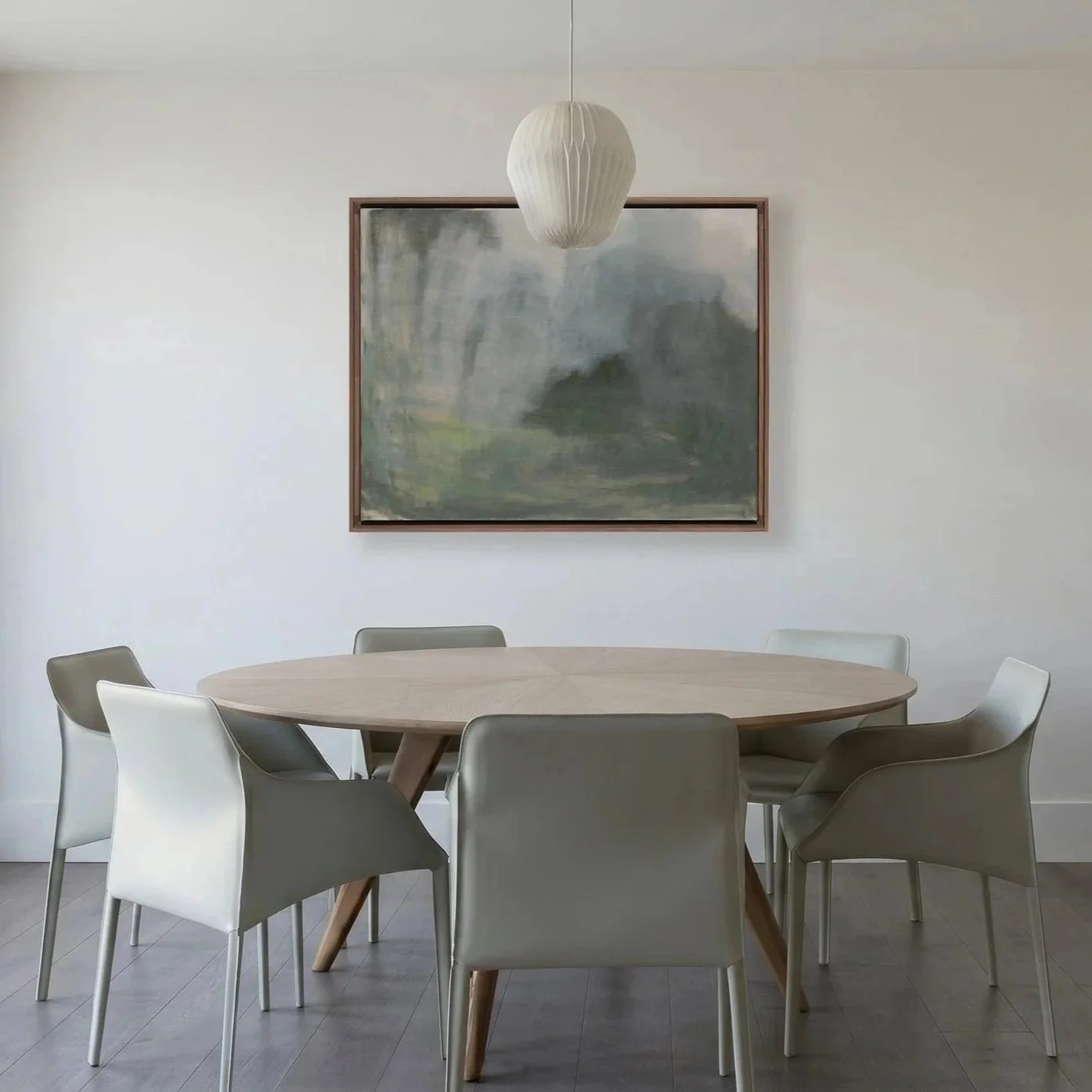 Minimalist dining room with a round wooden table and six modern chairs in neutral colors, a large abstract landscape painting on the wall, and a white paper lantern pendant light hanging above the table.