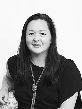 Black and white portrait of a woman with long dark hair, wearing a black top and a necklace, smiling softly.