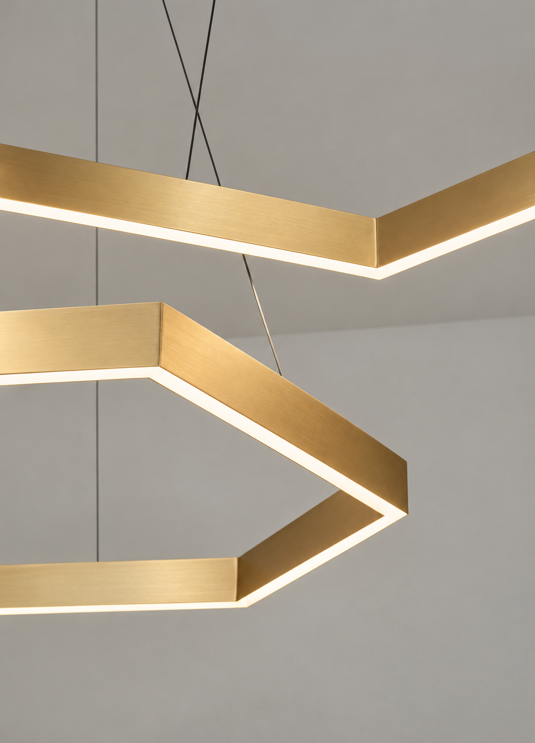 Close-up of modern geometric ceiling chandelier with rectangular gold frames and LED lighting, suspended by black wires against a plain ceiling.
