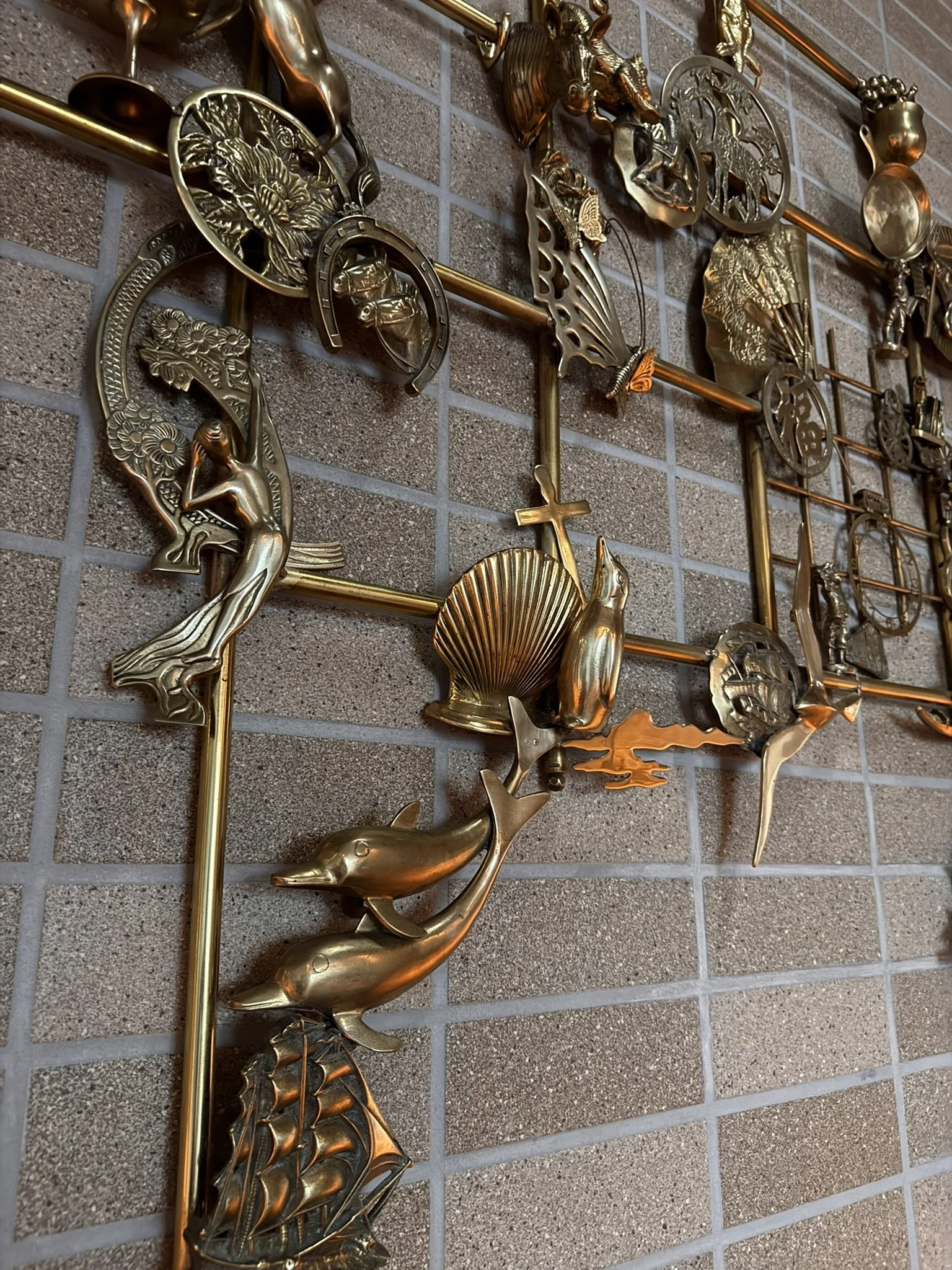Close-up of a decorative metal wall art featuring various animals such as dolphins, horses, a seahorse, a butterfly, and a shell, mounted on a brick wall.