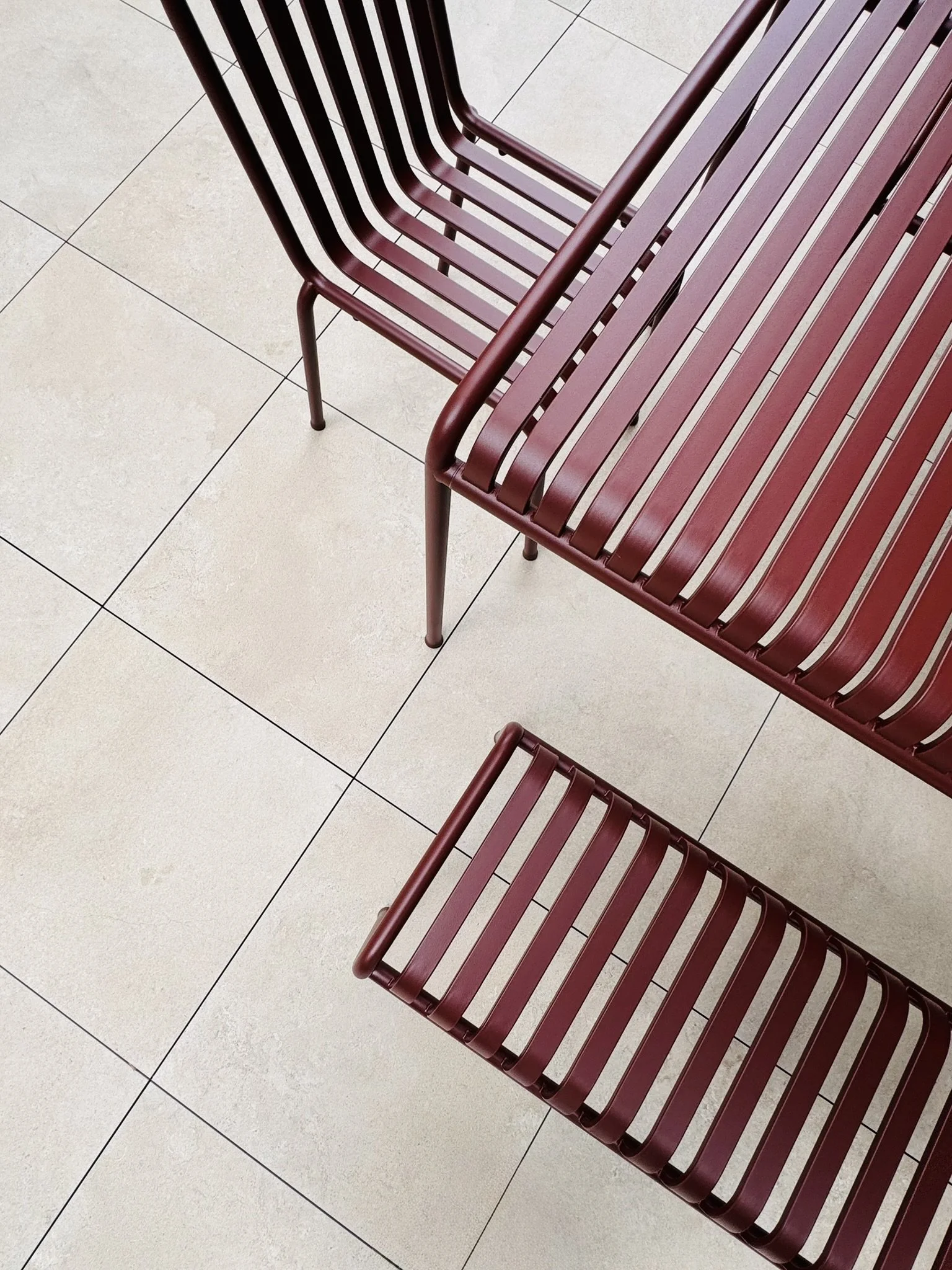 Two maroon metal chairs with slatted seats and backs, viewed from above on a tiled floor.