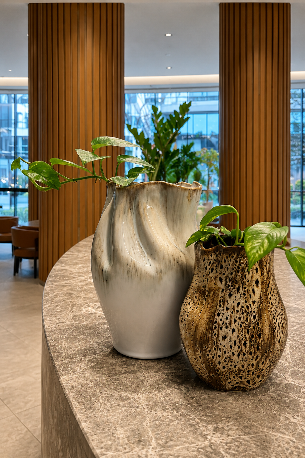 Two decorative vases with green houseplants on a marble table in a modern interior with wooden paneling and large windows.