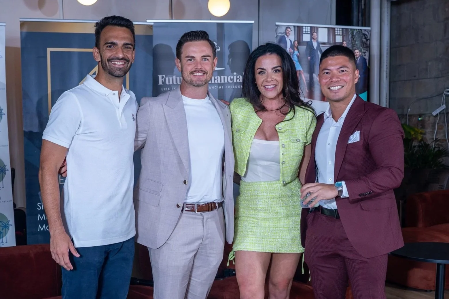 Four people, two men and two women, standing together at a professional event indoors, smiling at the camera, with banners in the background.