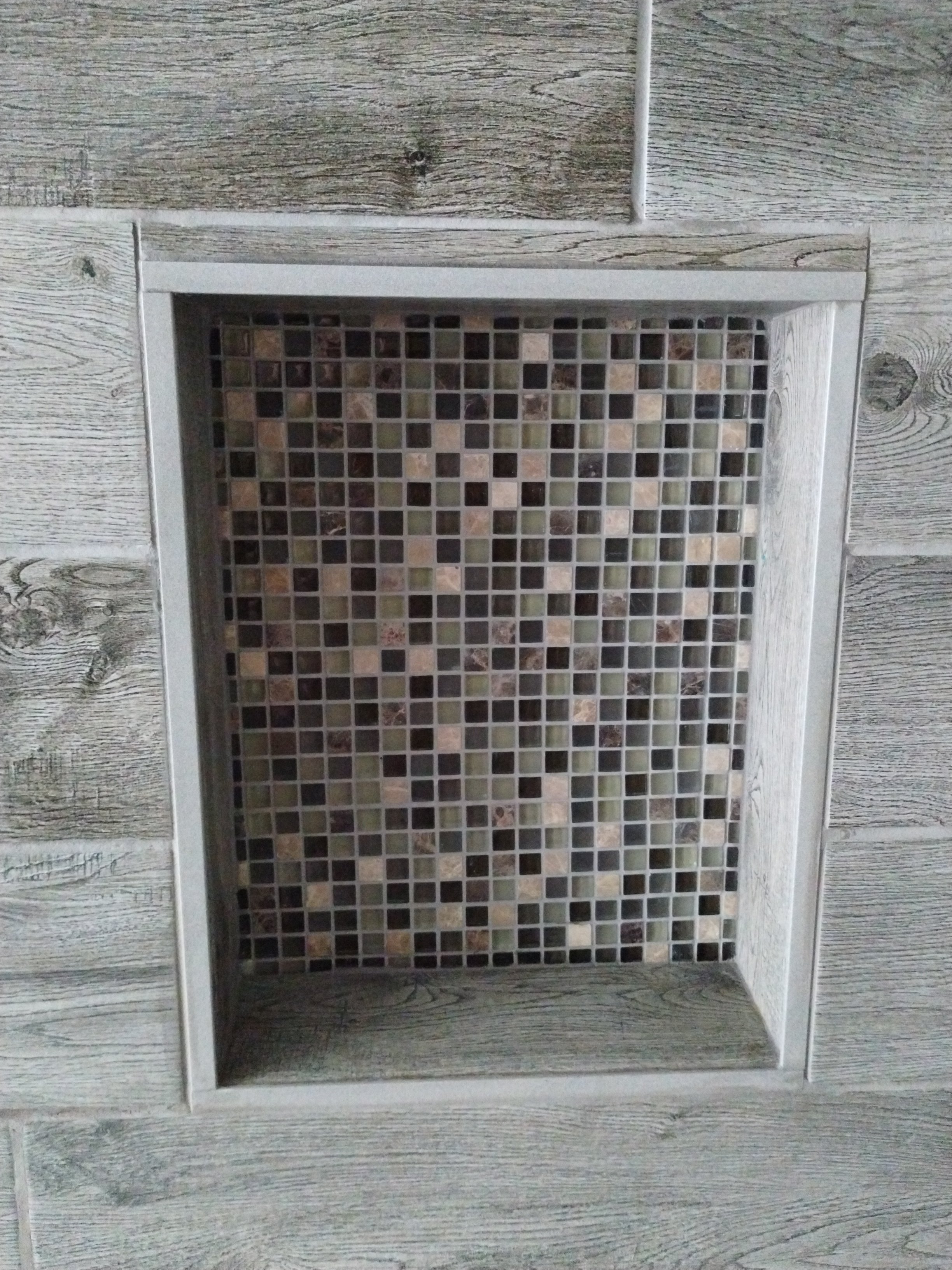 A built-in shower niche with aluminum trim and mosaic tile, set into weathered wood tile.