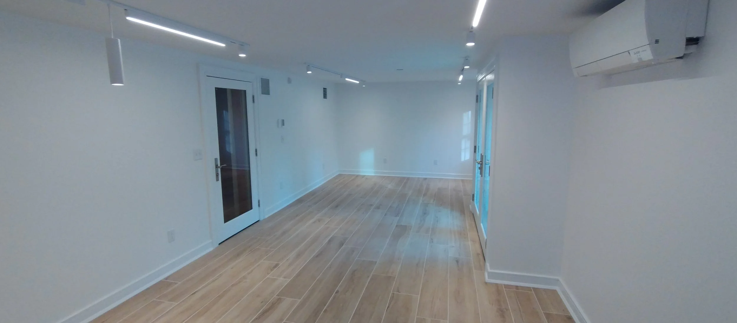 Sound proof home theater room with light wood floors, white walls, French doors with blue tint, ceiling lights, and a mini-split air conditioning unit.