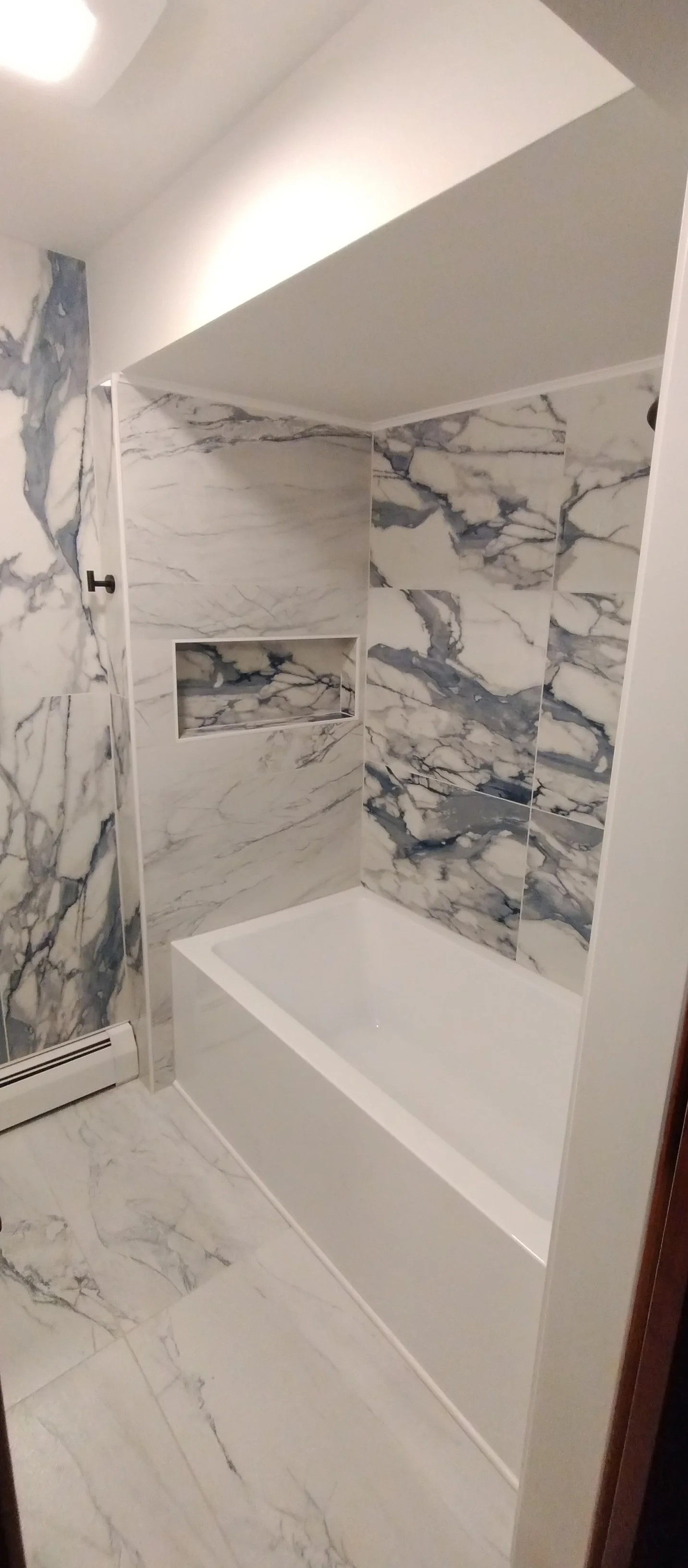 White deep tub with large format tile and black matte shower head, tub filler and grab bar.