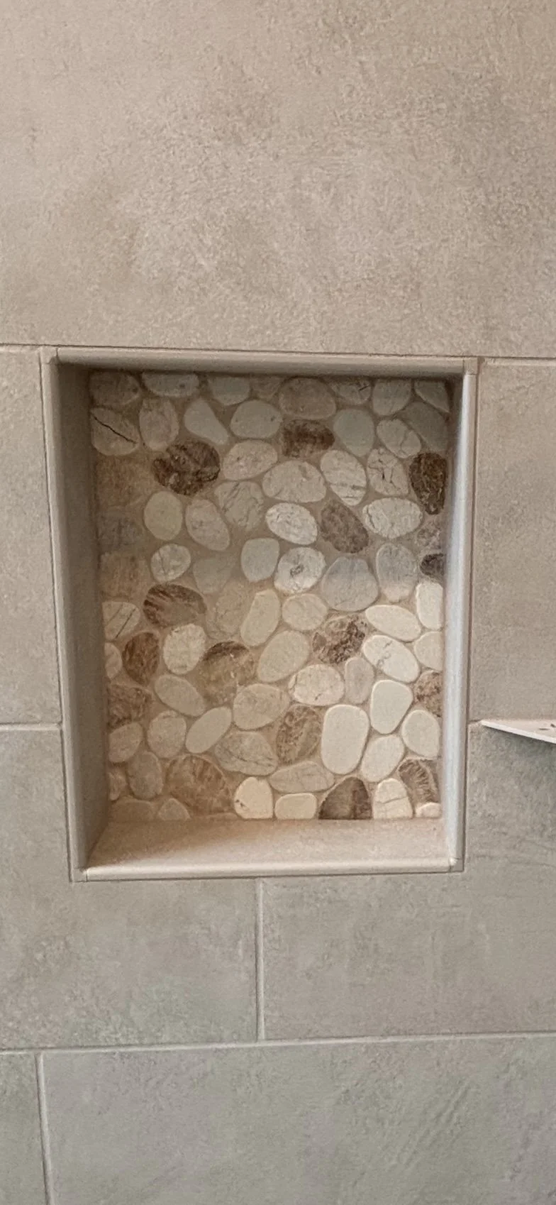 Bathroom shower niche with pebbles behind a beige tiled wall.