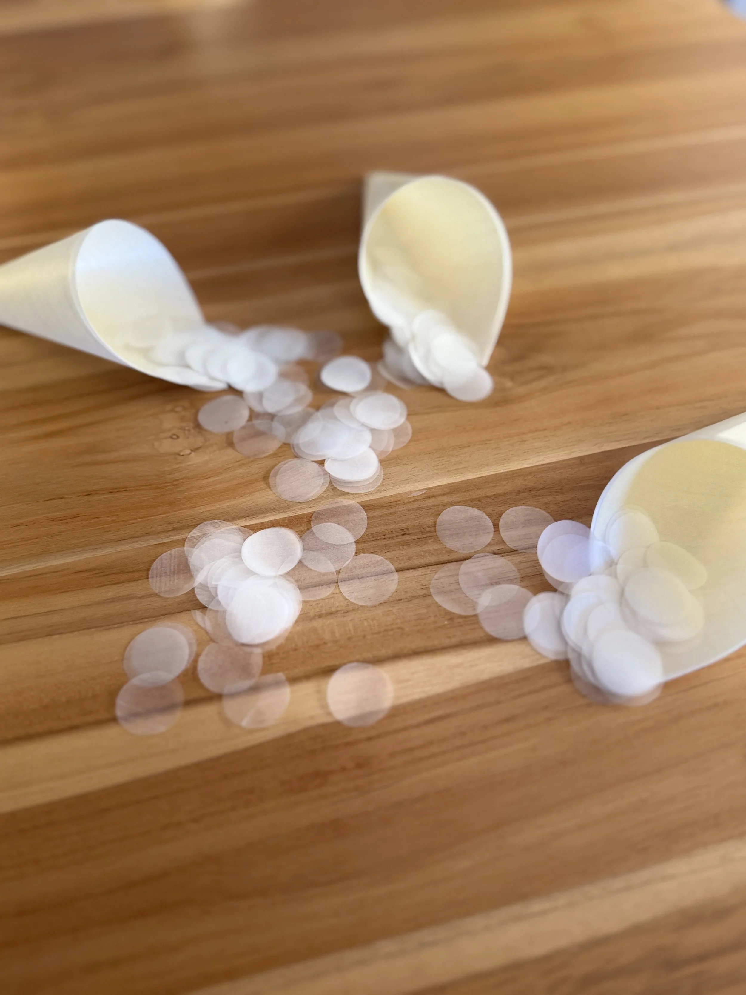 Spilled white paper confetti from paper cones on a wooden surface.