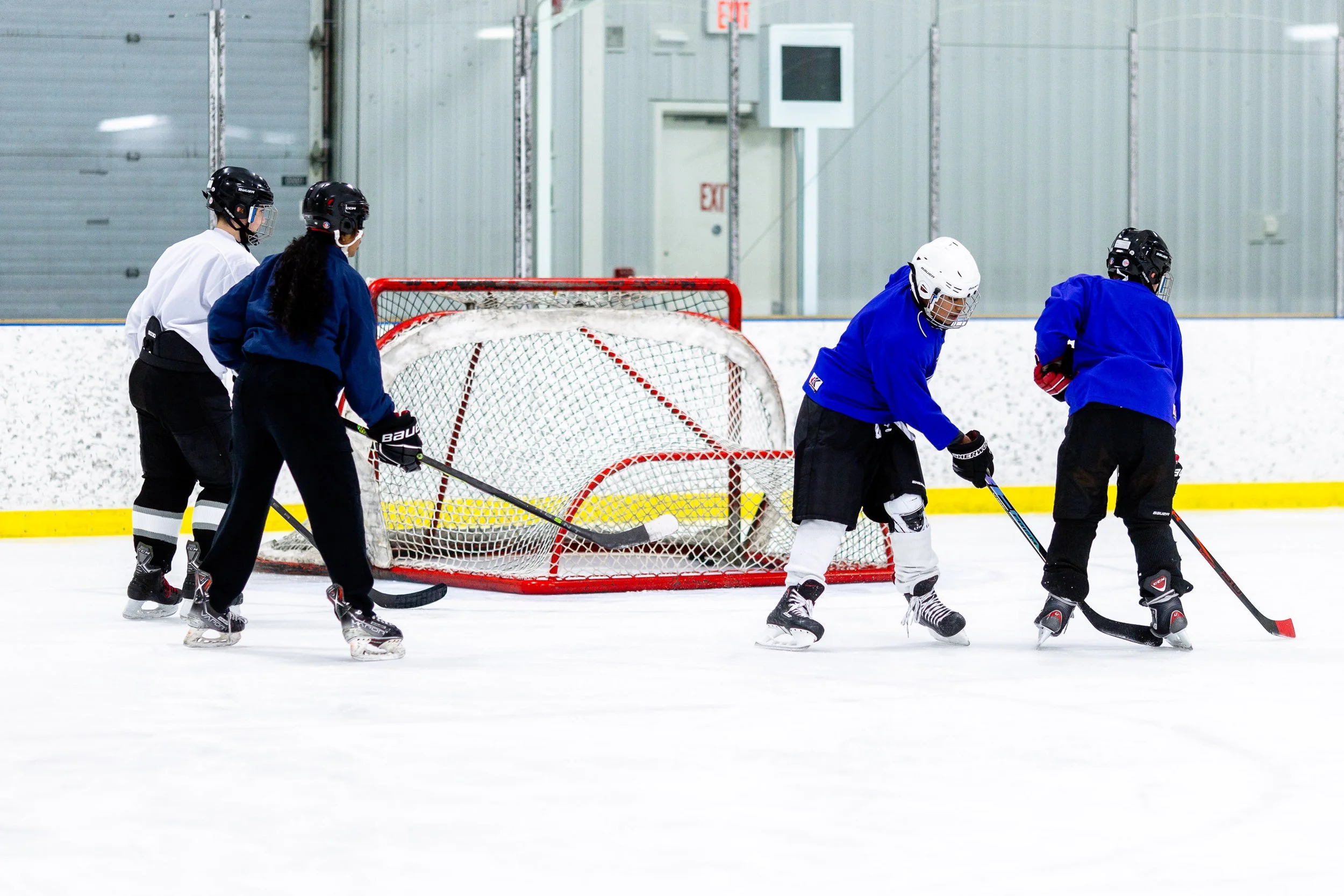 Multiple hockey players on a community rink practicing drills in bright blue and white jerseys.