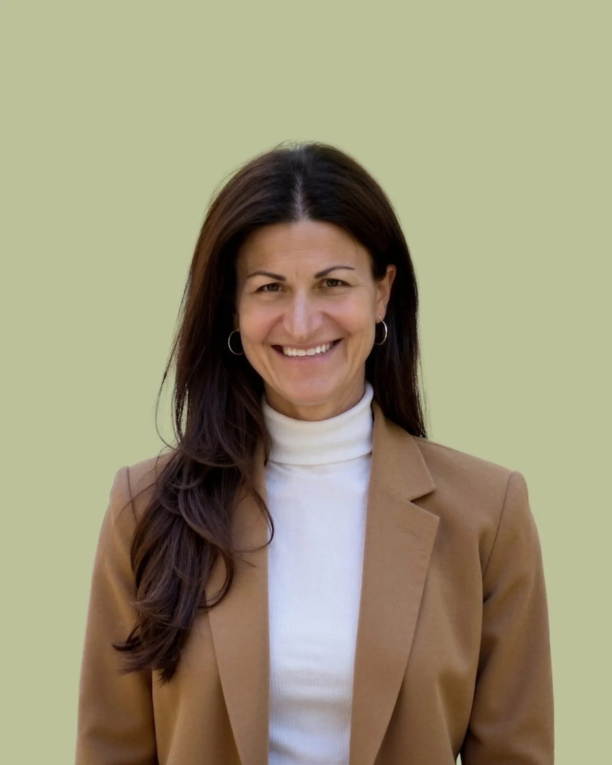 A woman with long brown hair, wearing a light pink sweater and gold earrings, smiling at the camera against a light green background.