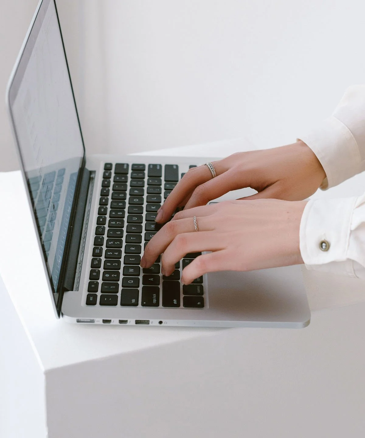 Person wearing white shirt typing on a laptop keyboard.