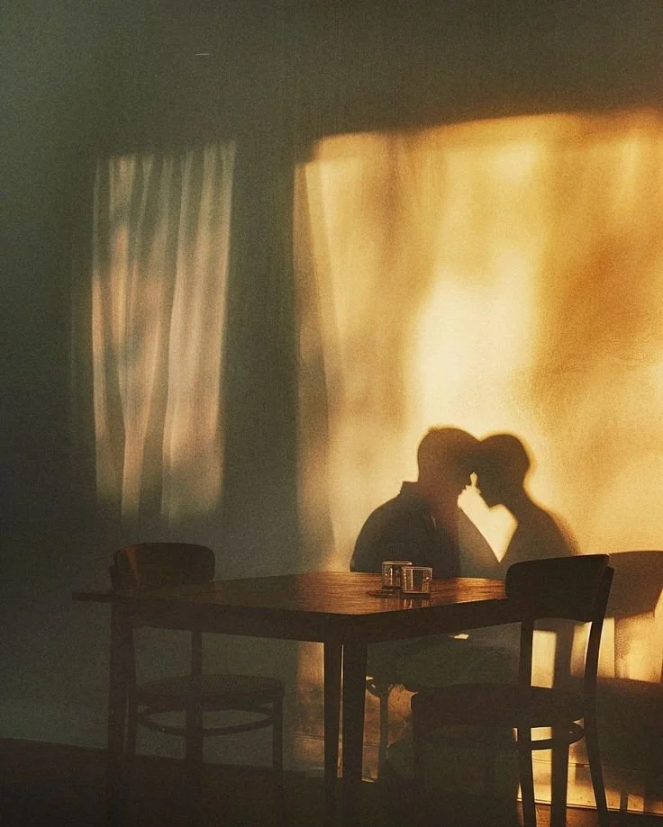 Silhouette of a couple sitting close together at a table with a warm, glowing curtain in the background