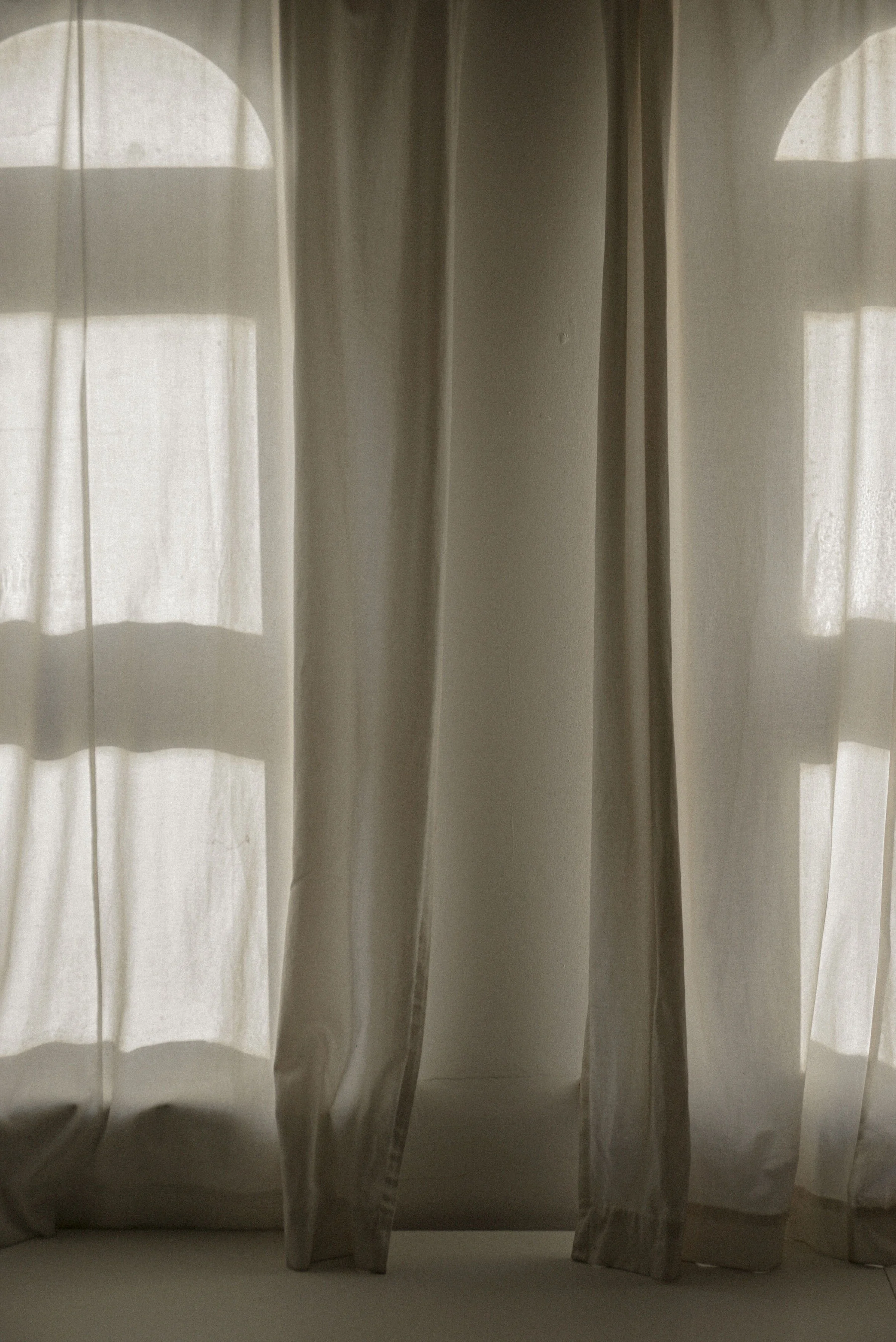 Light-colored curtains with sheer and opaque sections, allowing sunlight to filter through.