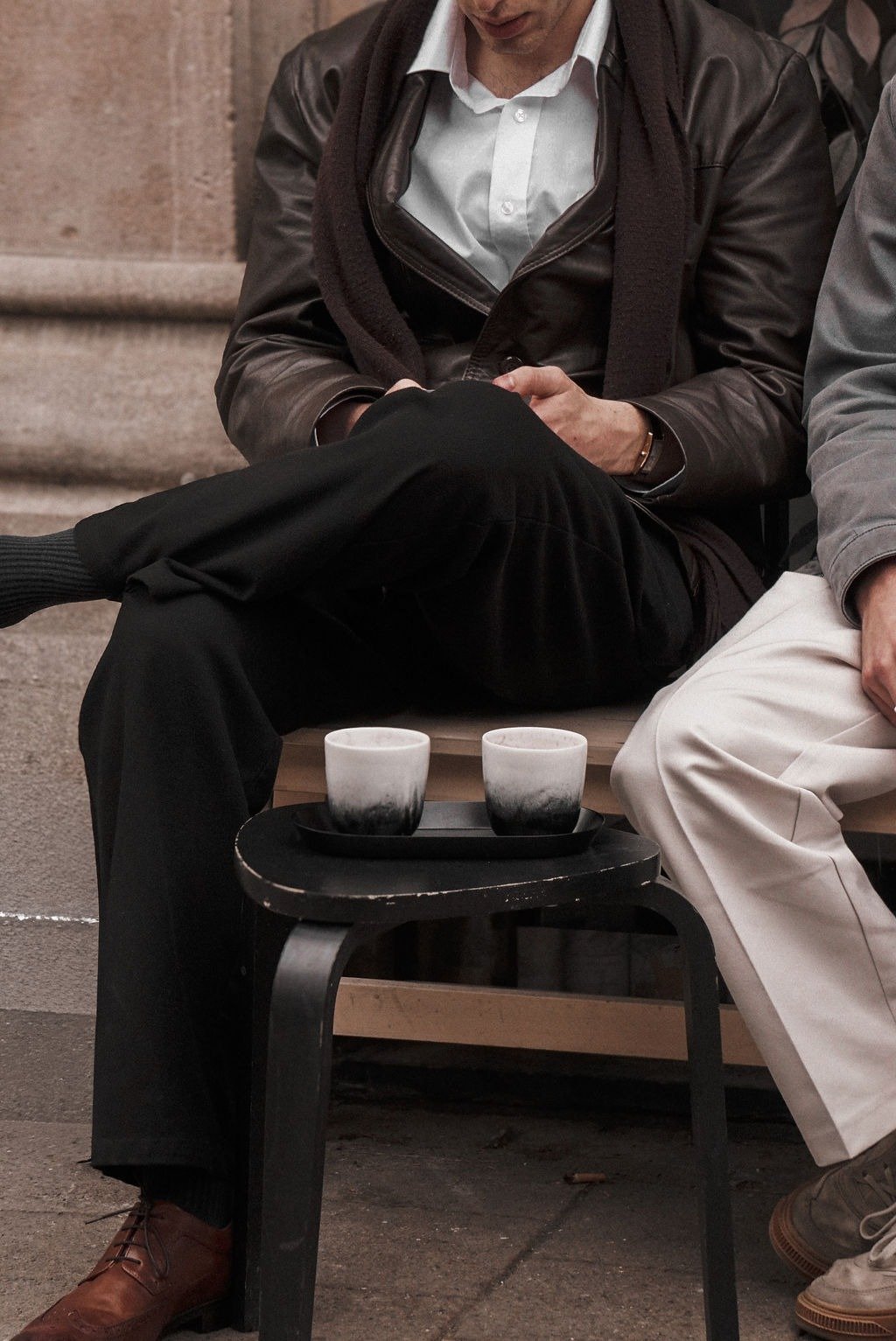 Two people sitting on a bench with a small black table holding two ceramic cups.
