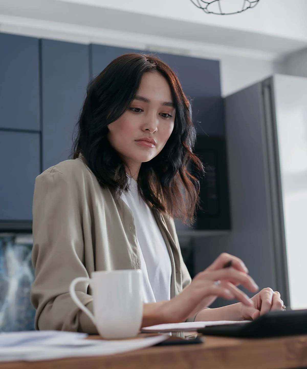 A woman with dark, wavy hair working on a keyboard at a desk in a modern kitchen.