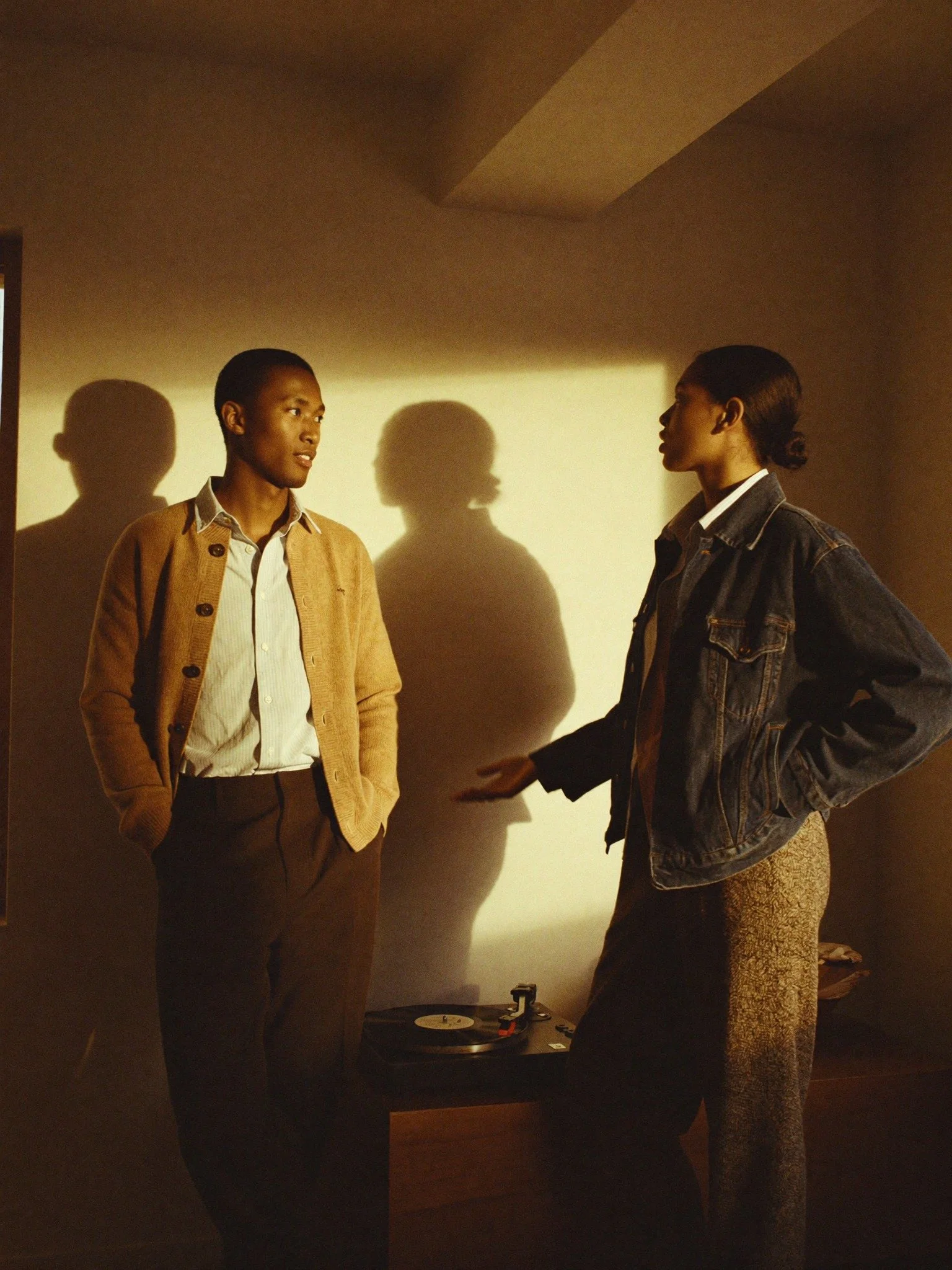 Two women are facing each other in conversation in a dimly lit room with a turntable on a table nearby.