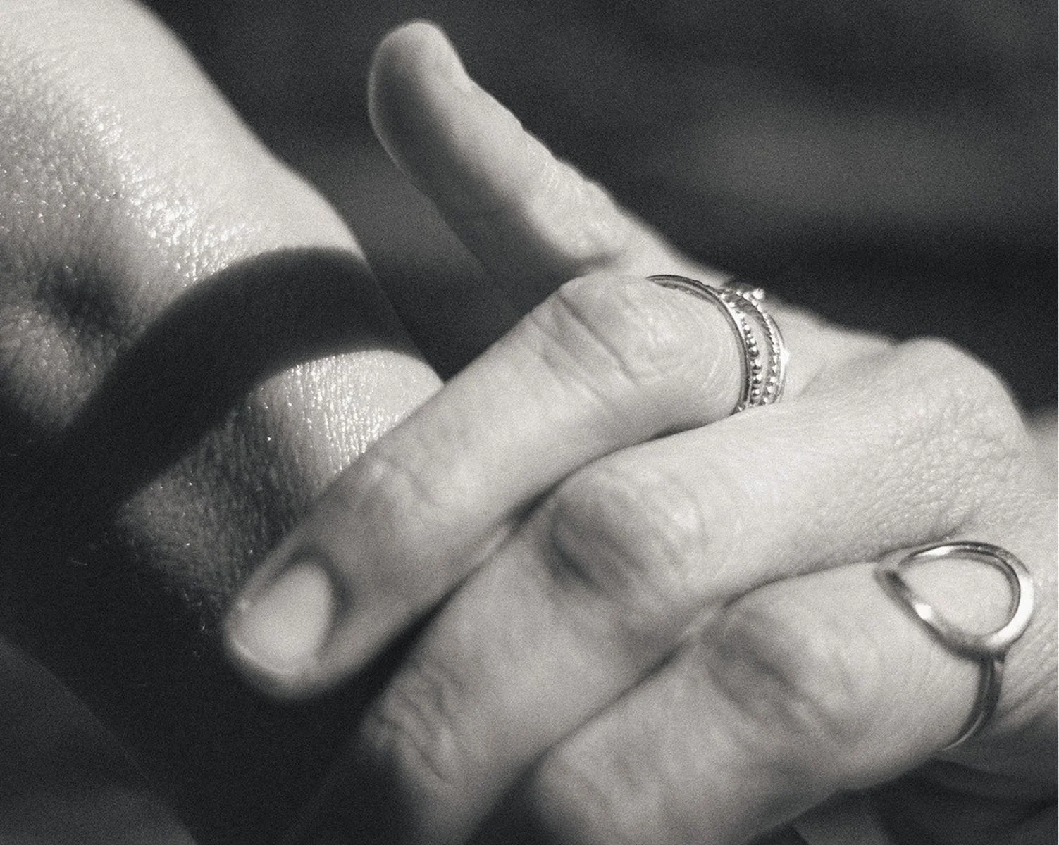 Close-up of a person's hand with rings, touching their lips, with dramatic lighting and shadows.