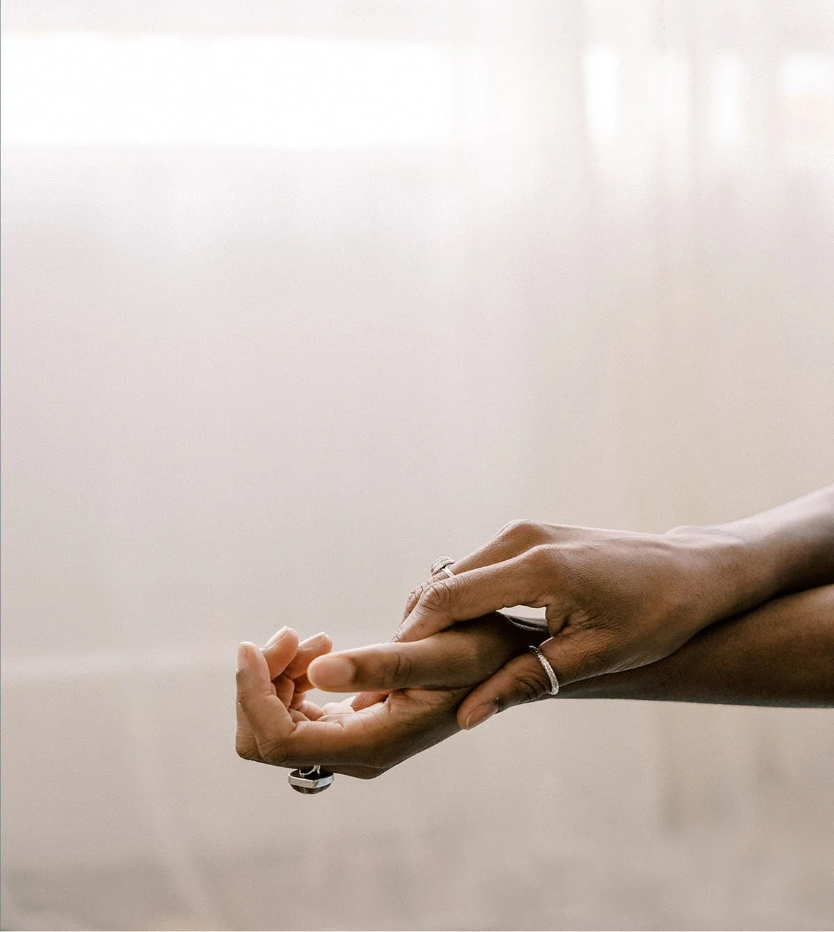 Close-up of two hands gently holding each other, with one hand supporting the other, against a plain, soft background.