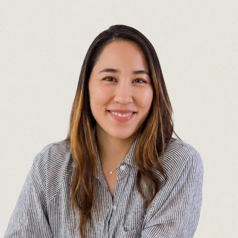 A woman with long brown hair smiling, wearing a striped shirt, against a plain white background.