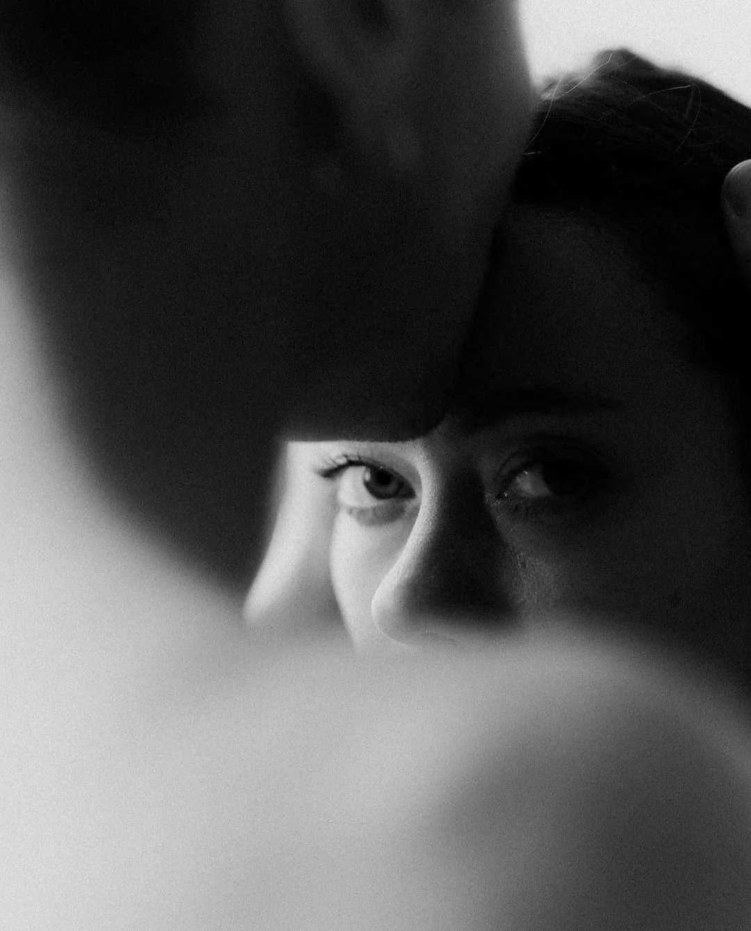 A black and white photo of a woman looking into a mirror, partially obscured by her arm.