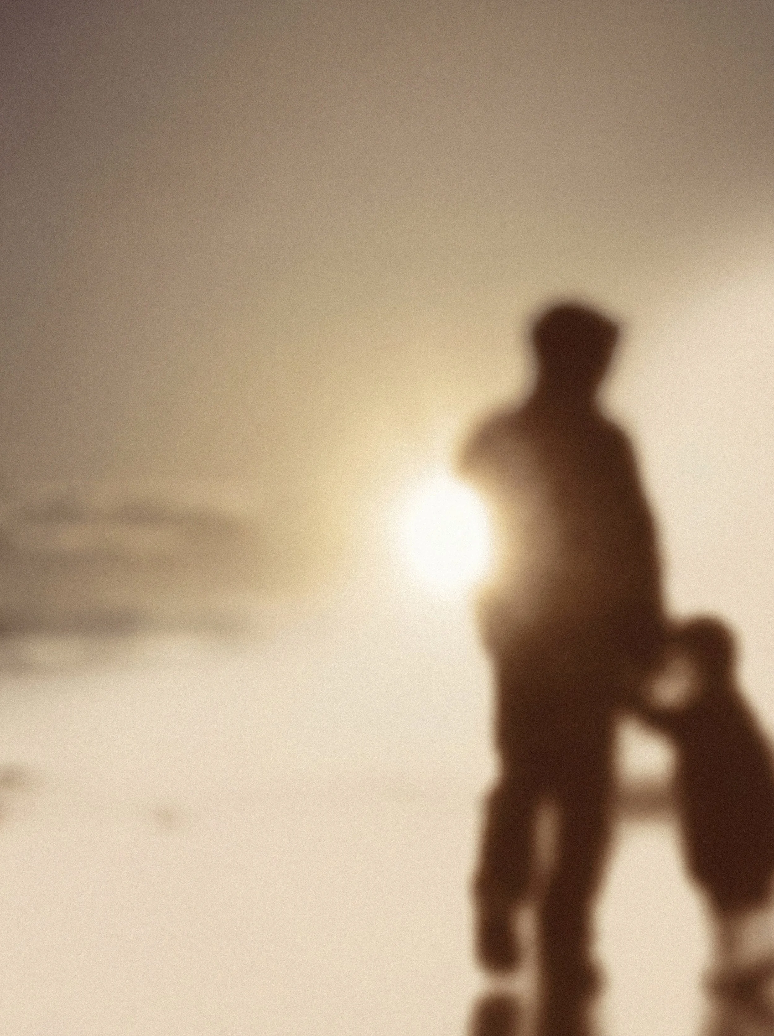 Blurred silhouette of a person, possibly male, standing against a light-colored background with a bright light source behind them.