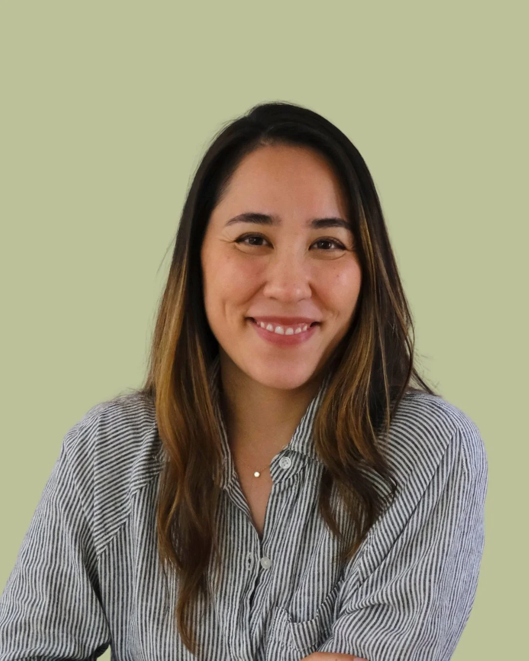 A young woman with long brown hair wearing a white turtleneck sweater looking at the camera with a slight smile, against a light green background.
