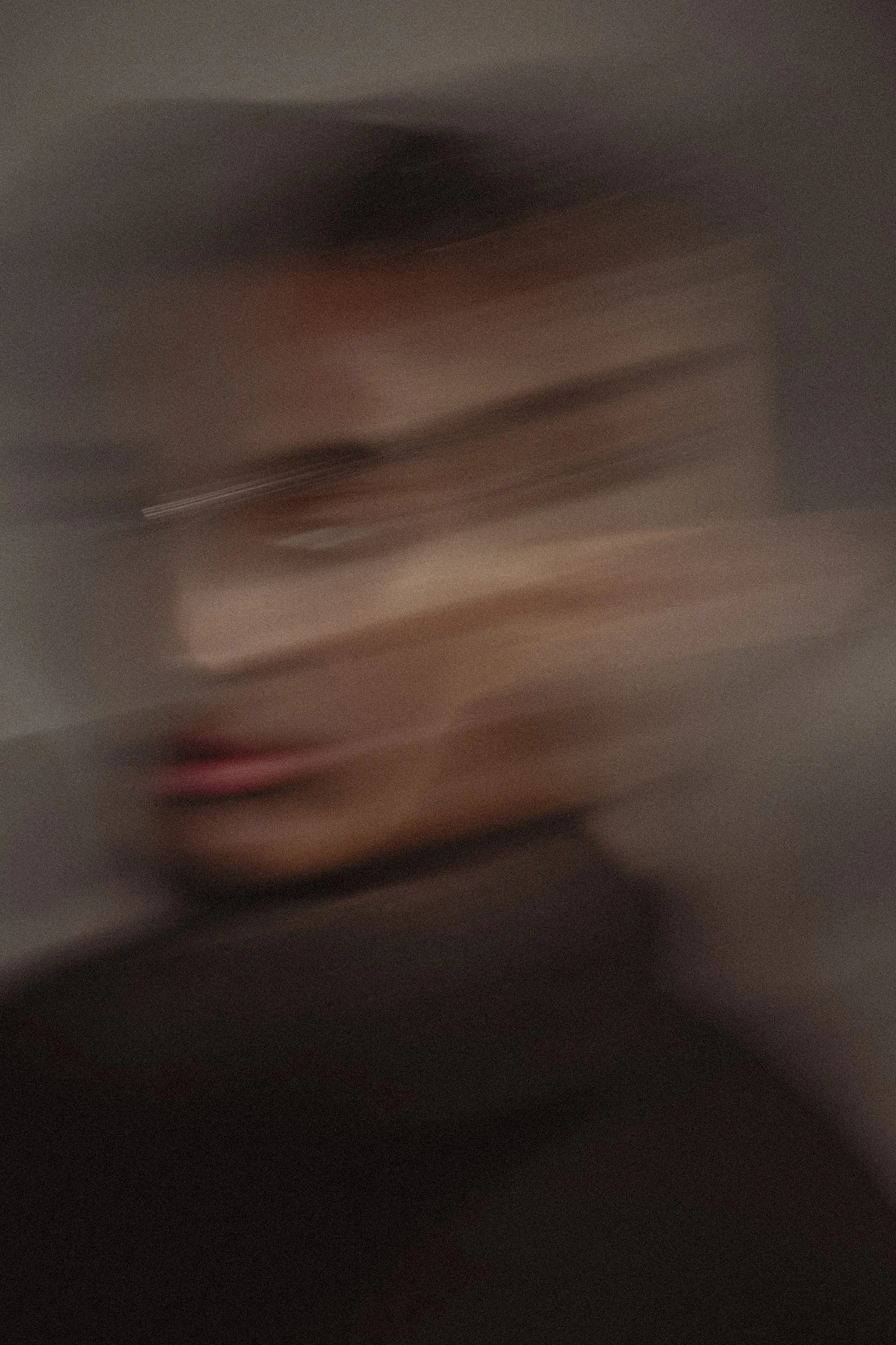Blurred image of a person's face with dark hair, pink lips, and light skin, with motion blur creating a streaked effect.