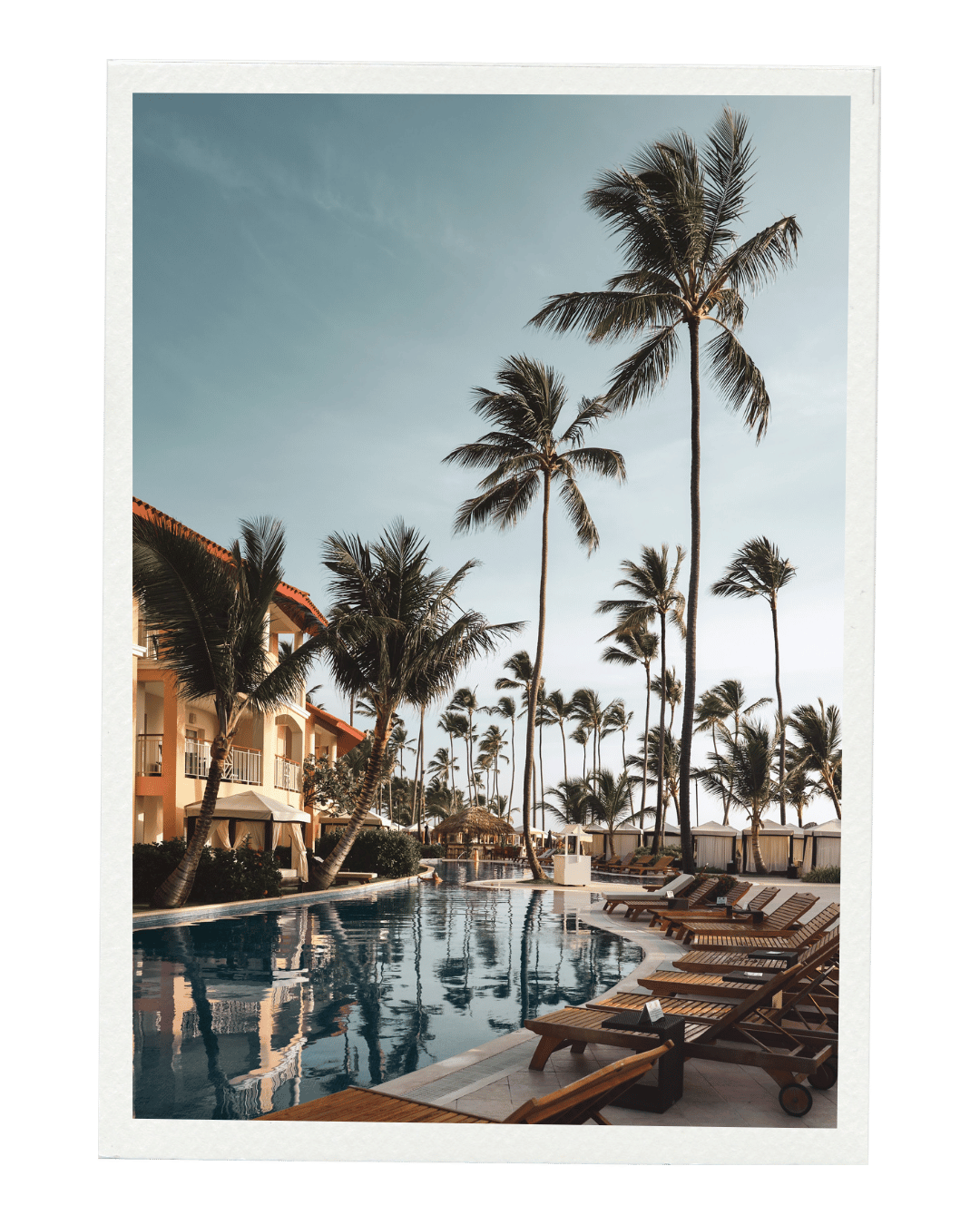 Swimming pool surrounded by palm trees and resort buildings under a clear sky.