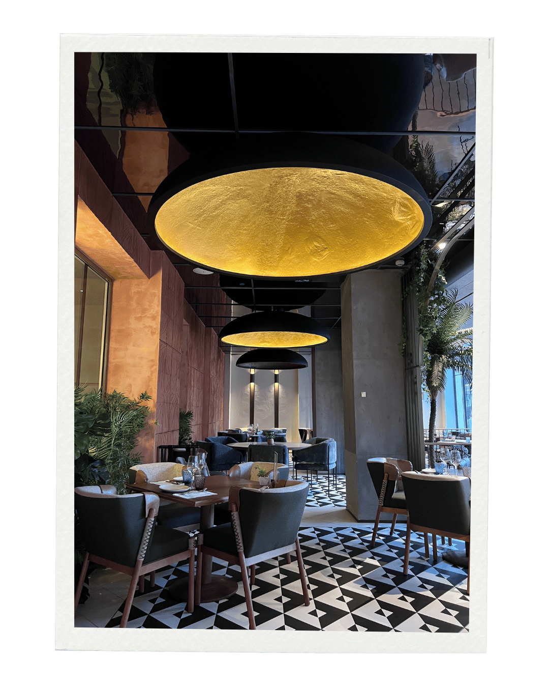 Interior of a restaurant with black and gold ceiling lights, patterned black-and-white floor, and modern furniture including chairs and tables.
