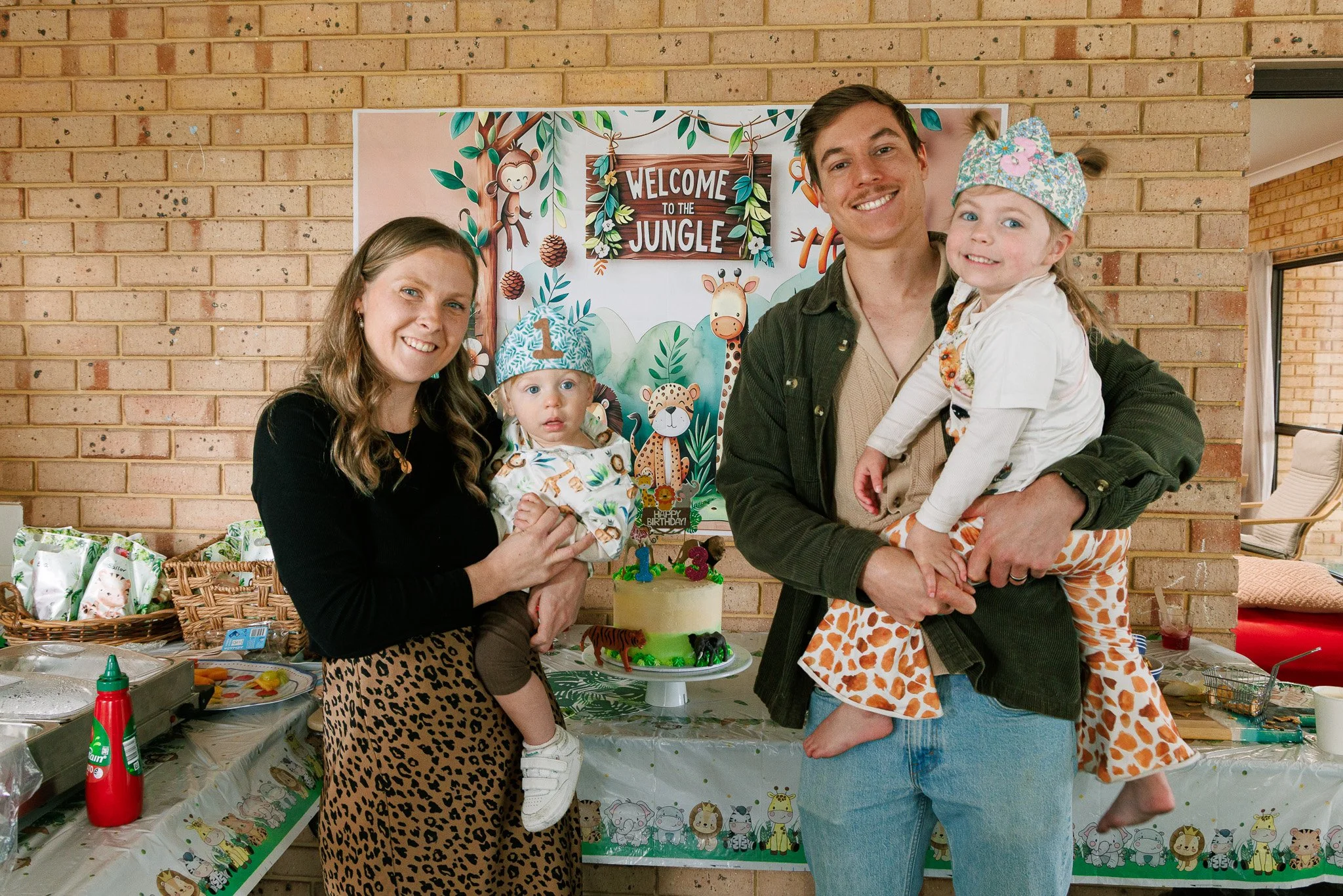 Family at a jungle-themed birthday party with children, cake, and decorations.