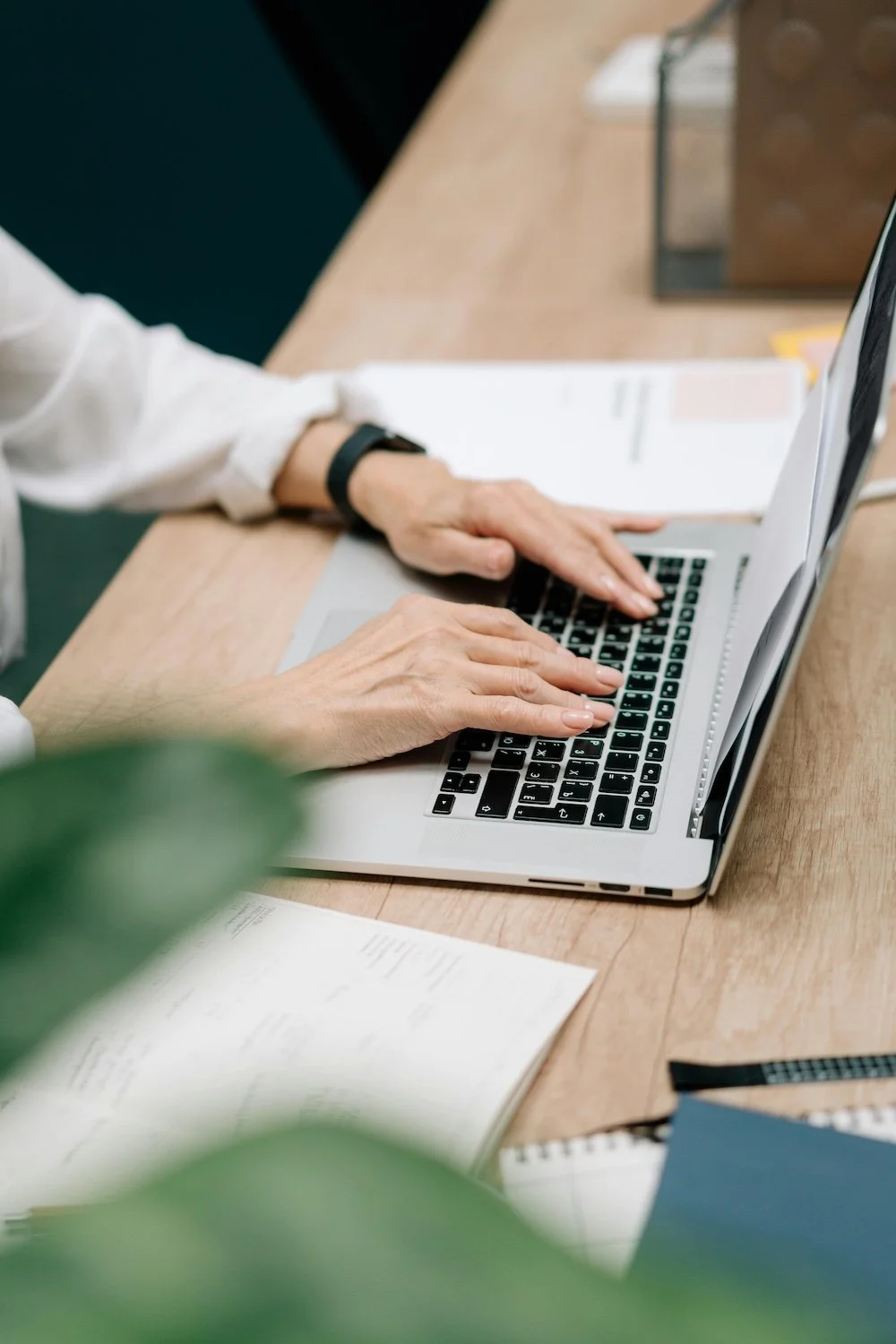 A Macbook laptop on a desk with a woman's hands typing on it