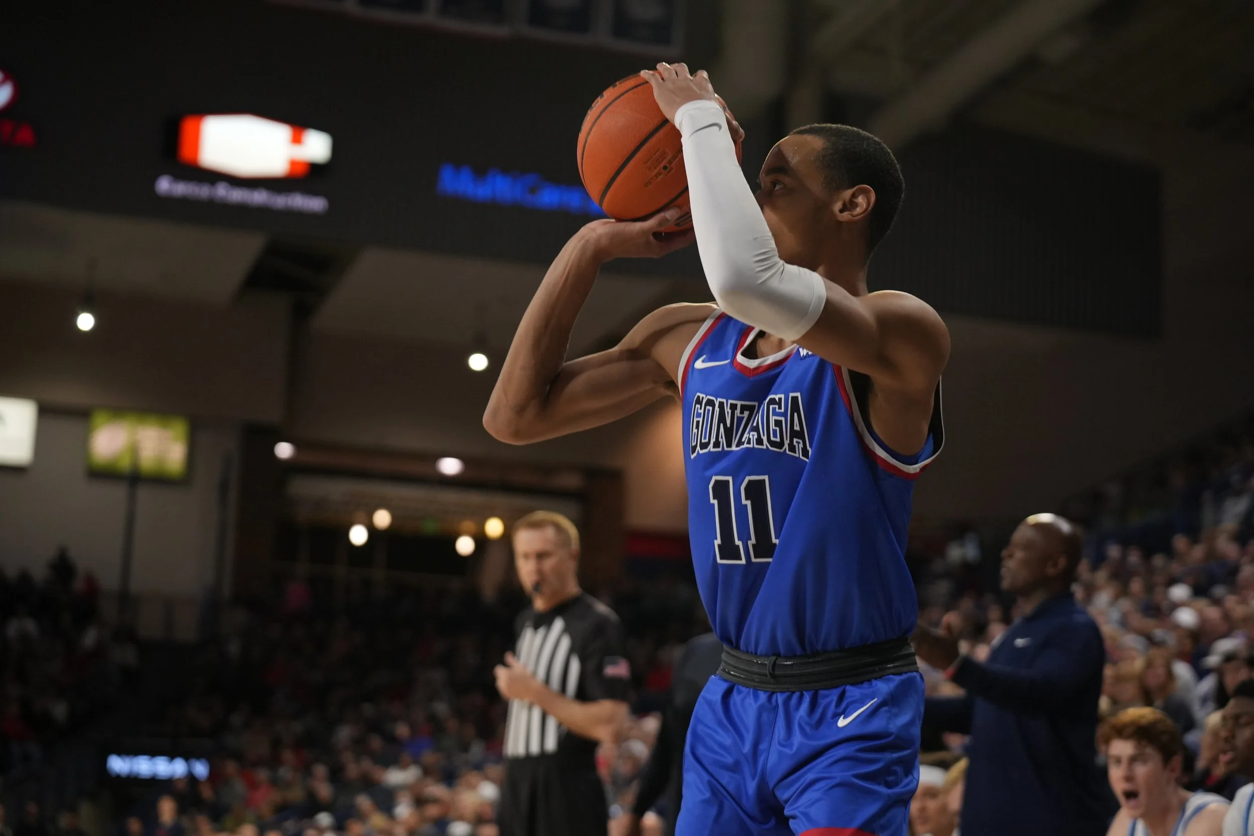 Basketball player in blue Gonzaga jersey taking a shot in a stadium.