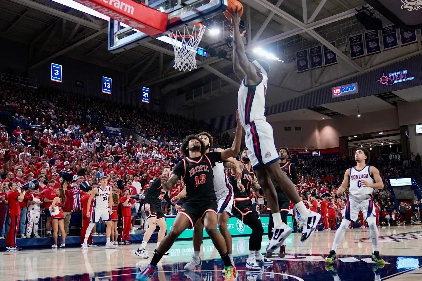 Basketball players from Gonzaga and Pacific competing near the hoop in a crowded arena.