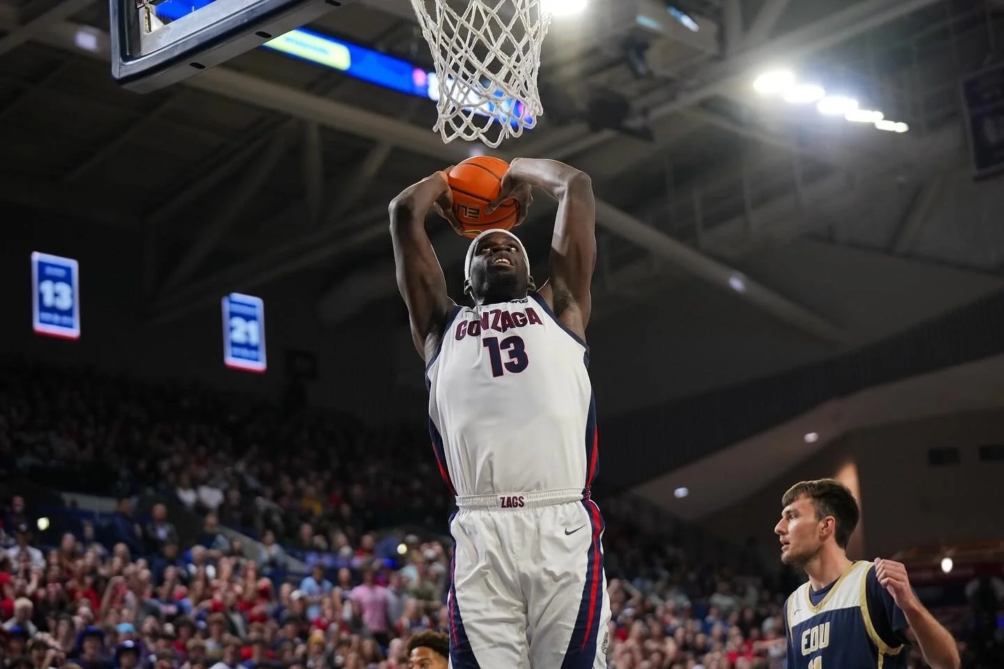 Basketball player in white jersey dunking a basketball during a game in a crowded indoor arena.