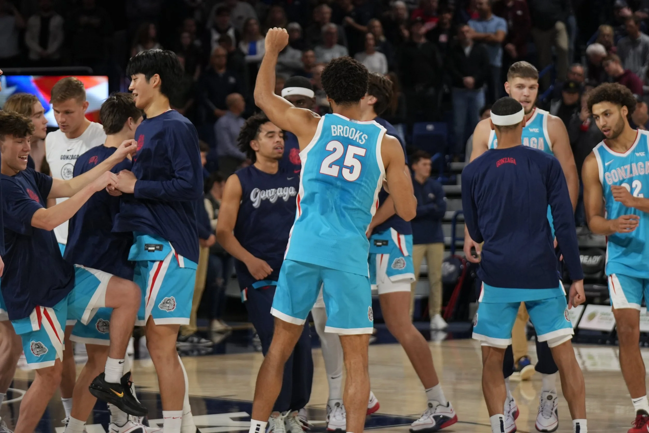 Basketball players wearing Gonzaga jerseys and warm-up gear, engaging in pre-game activities or celebrations on the court.