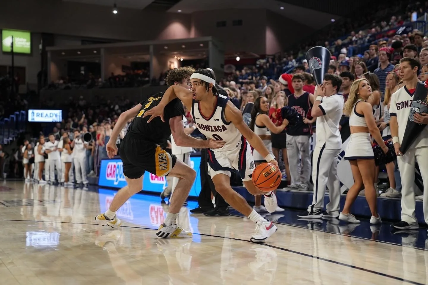 Basketball player dribbling during college game with cheering crowd in background.