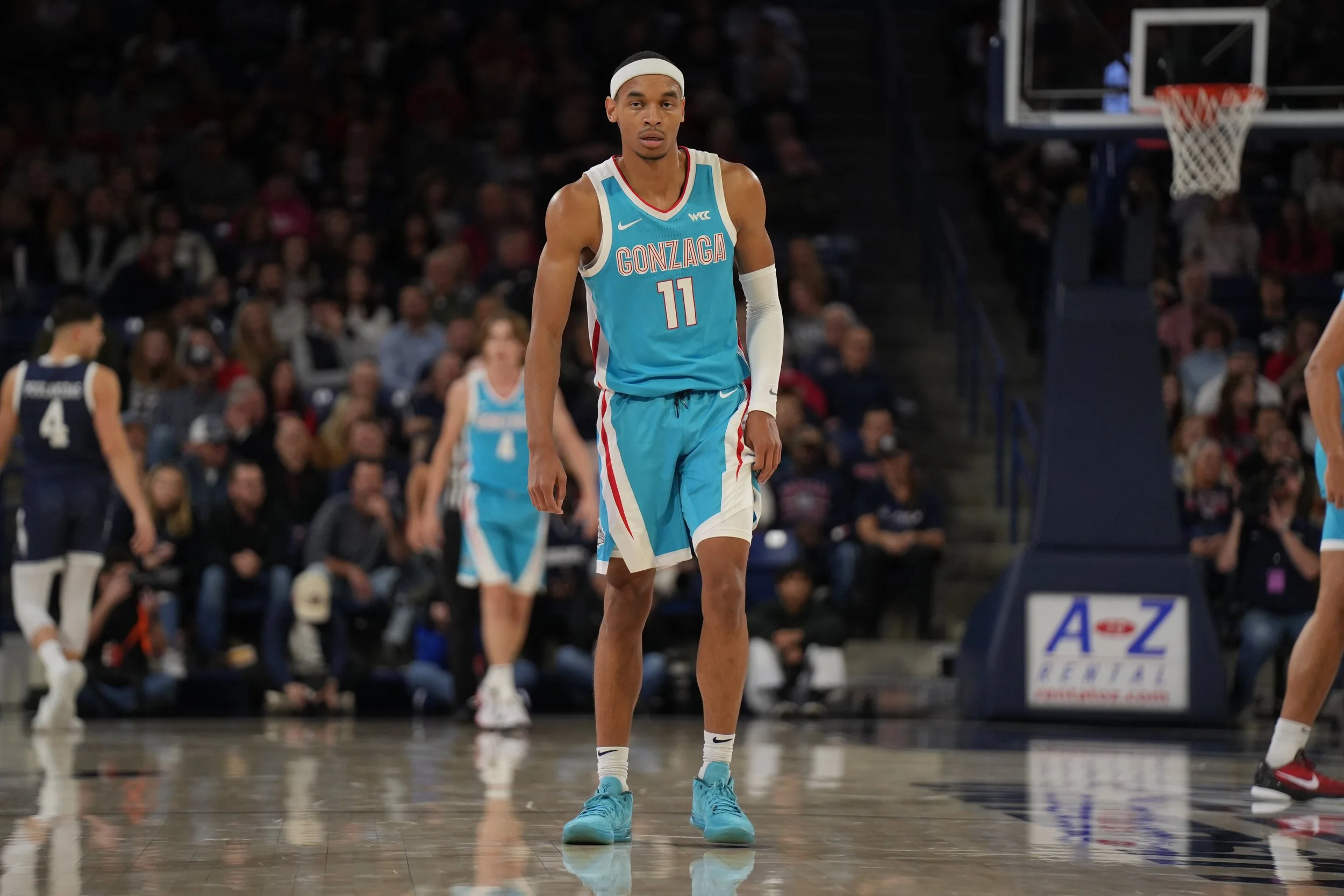 Basketball player in teal Gonzaga uniform on court during game, with audience in background.