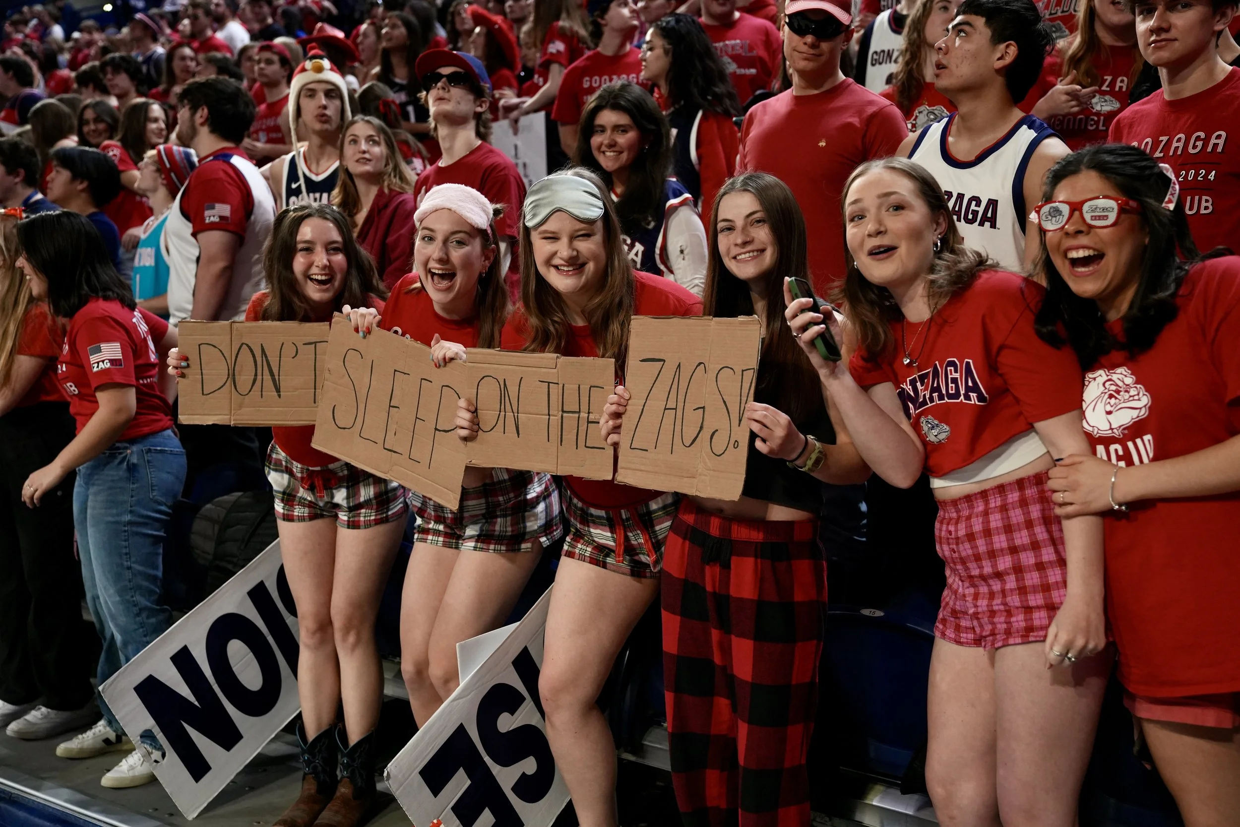 Group of enthusiastic fans wearing red and holding signs, attending a sports event, with a sign reading "Don't Sleep on the 'Zags!"