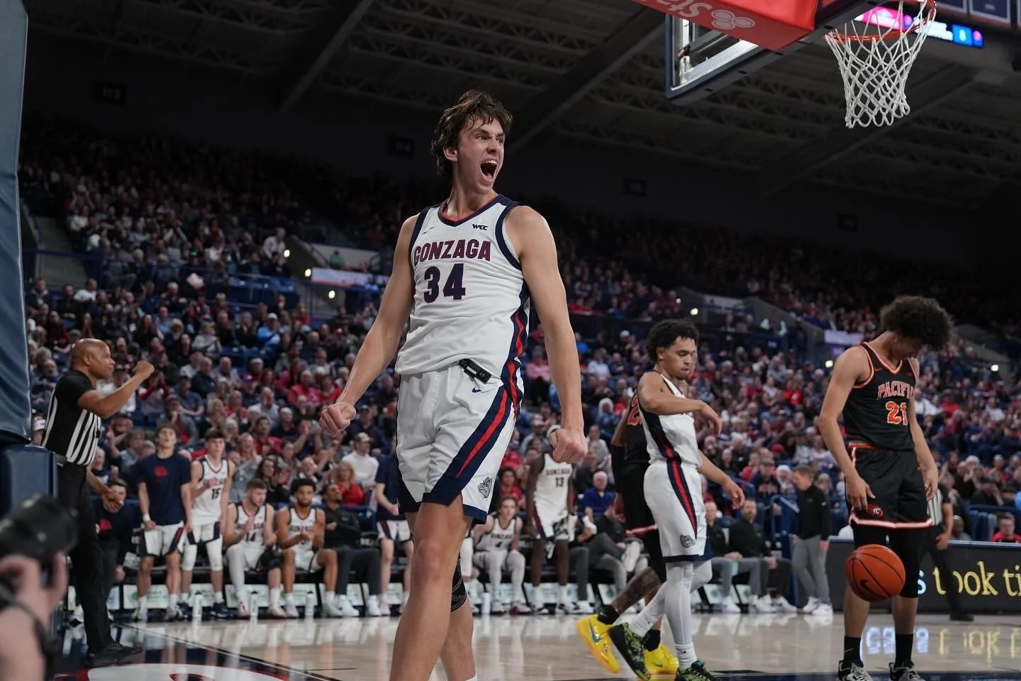 Basketball game with Gonzaga player celebrating on court, other players and referee nearby, audience in background.