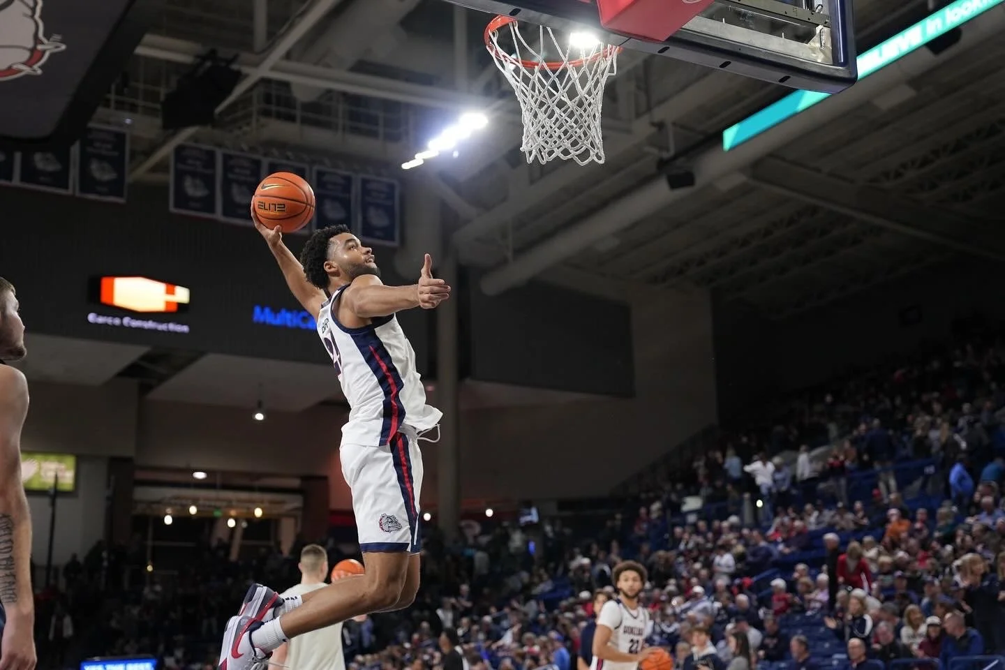 Basketball player jumping for a dunk in a game, with a crowd watching in an indoor stadium.