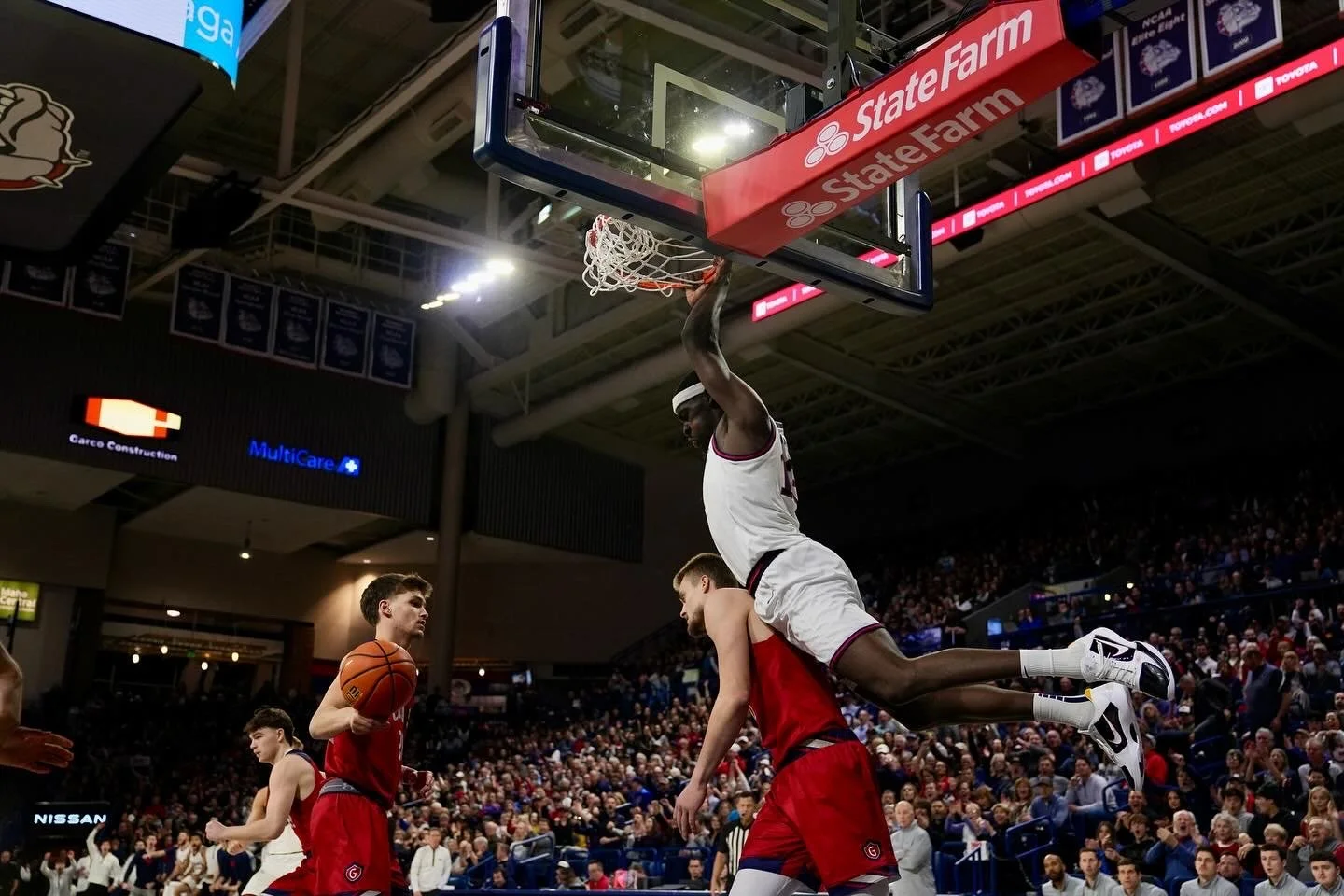 Basketball player dunking during a game with another player in the foreground.