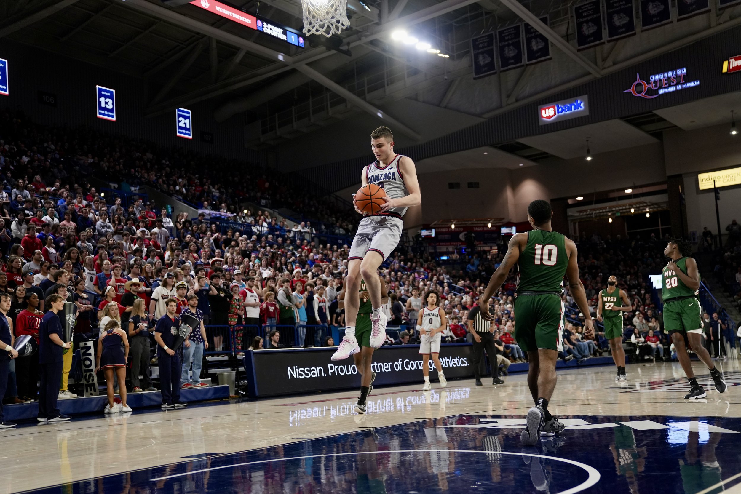 Basketball player from Gonzaga jumping and holding a basketball during a game in a crowded indoor arena.