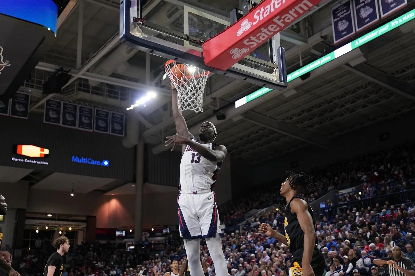 Basketball player in white jersey performing a slam dunk during a game, with spectators in the background.