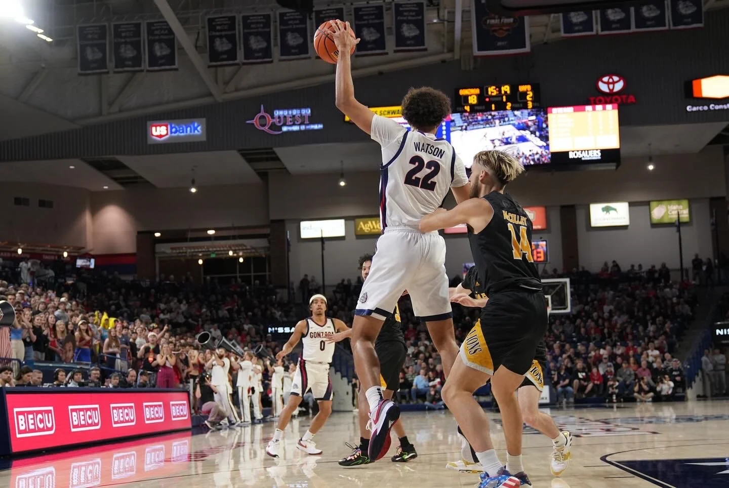 Basketball game with a player from Gonzaga wearing jersey number 22 jumping with the ball, another player from a different team nearby, and a crowd in the background.