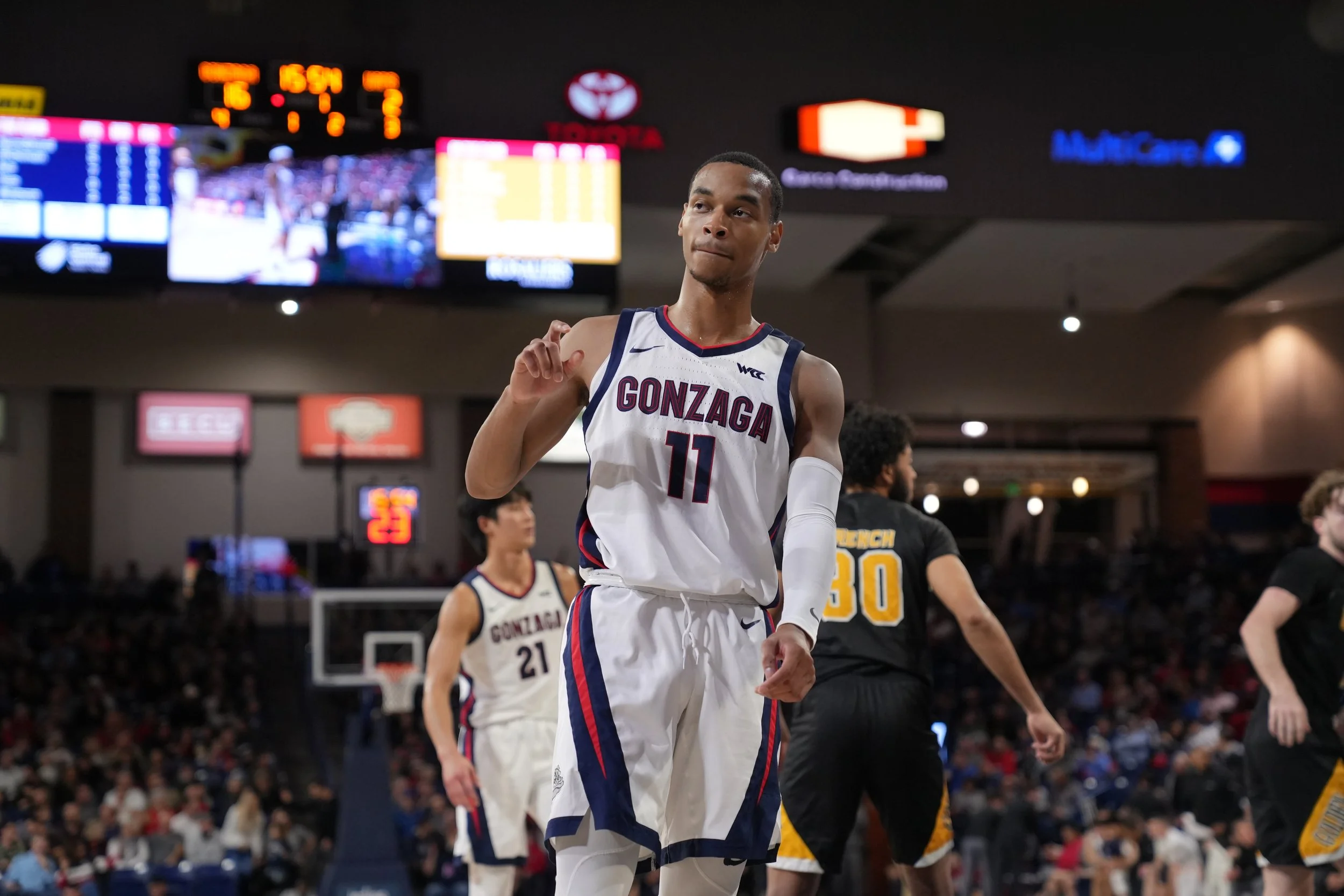 Basketball player wearing number 11 Gonzaga jersey, on court during game, with scoreboard in background.
