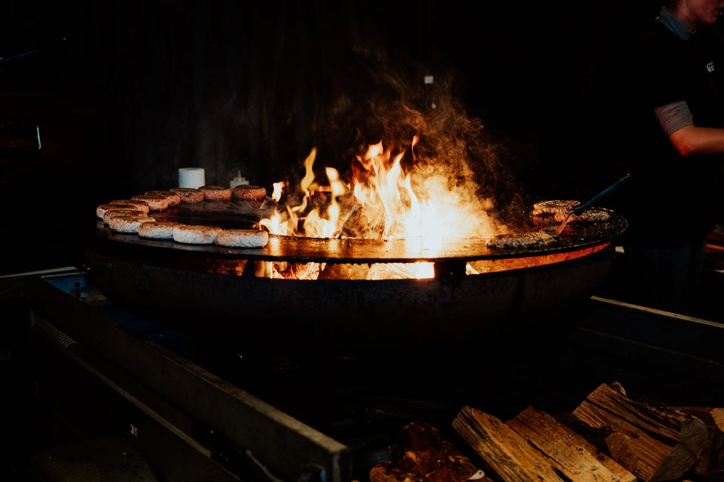 Grill mit brennenden Flammen, auf dem Fleisch und Burger Patties gegrillt werden.