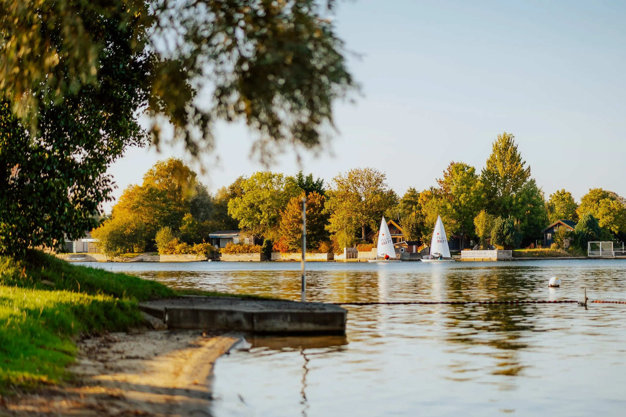 Der Blick auf einen Fluss mit Segelbooten und Bäumen in herbstlicher Farbe bei Sonnenuntergang.