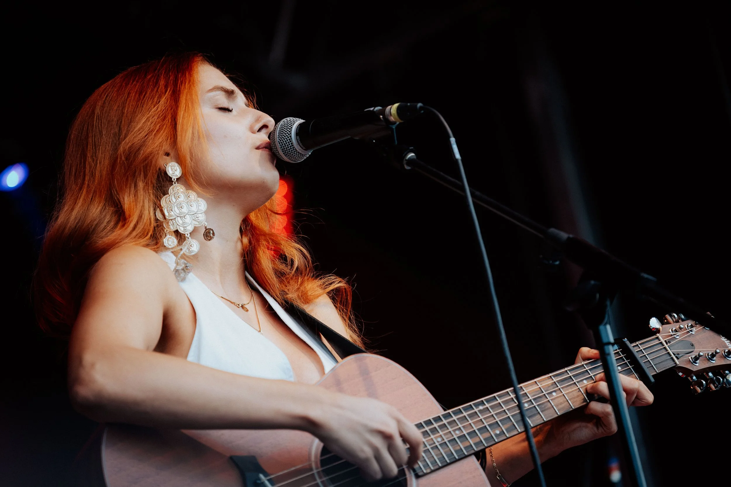Eine Frau mit roten Haaren, die Gitarre spielt und singt, während sie vor einem Mikrofon steht.
