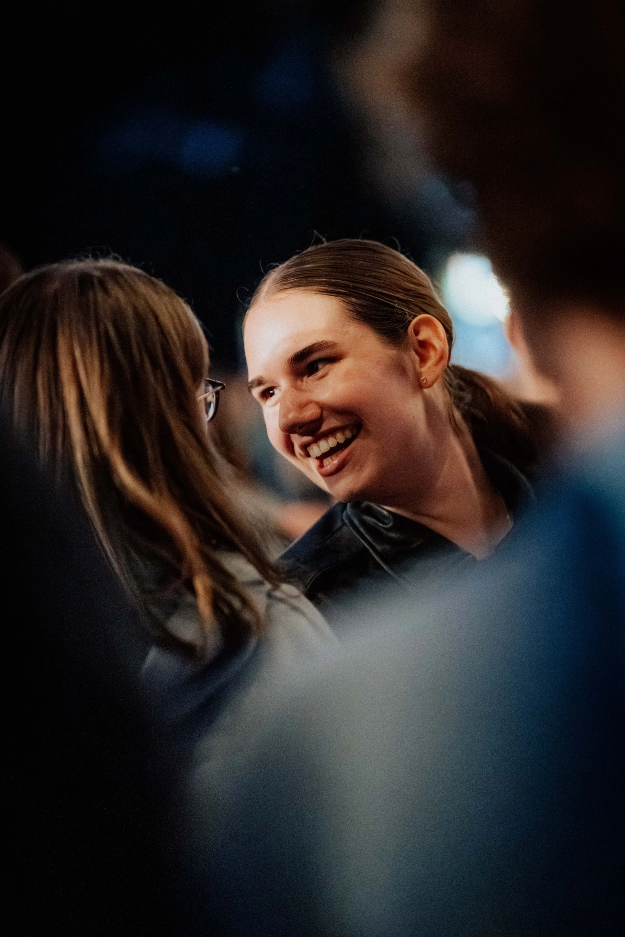 Zwei Frauen lachen und sprechen in einer engen Gruppe in einem dunklen Raum.