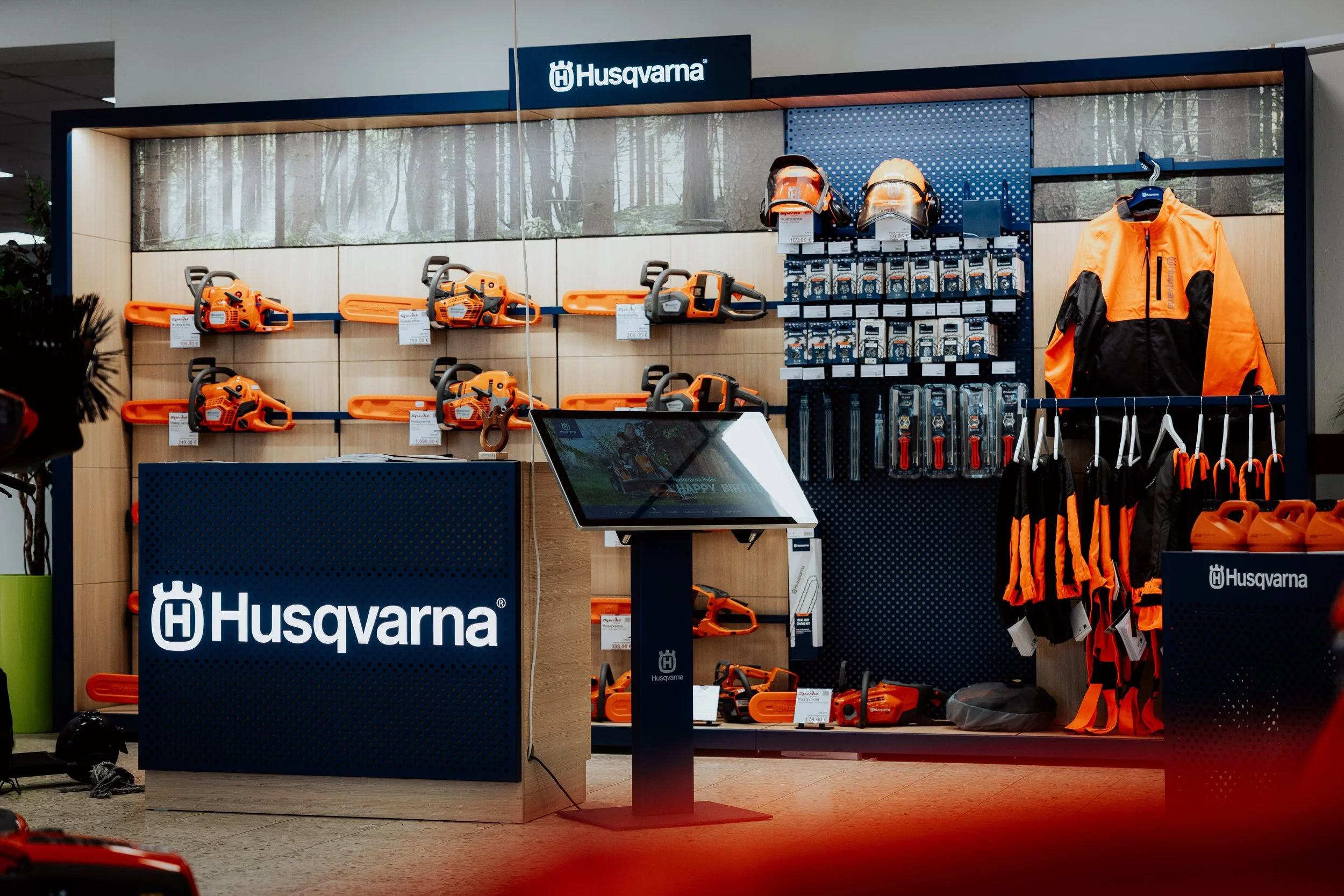 Husqvarna Verkaufsdisplay mit Kettensäge, Helmen und Schutzkleidung in einem Geschäft.